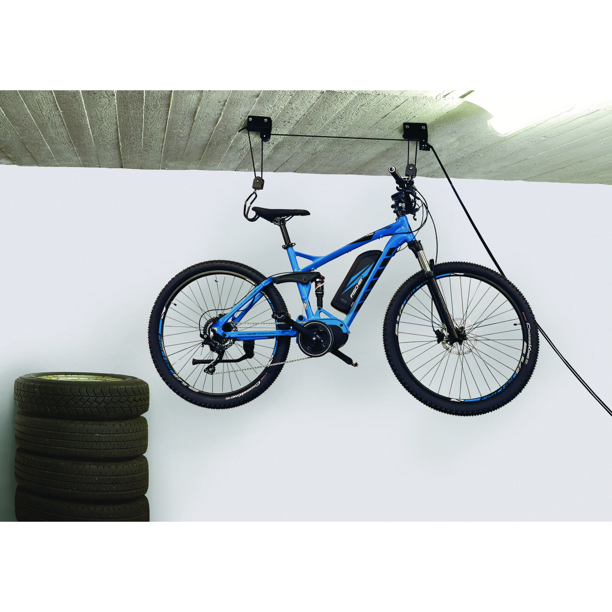 Blaues Elektrofahrrad, das von einer Decke abgehängt ist, neben einem Reifenstapel. Weißer und grauer Hintergrund.