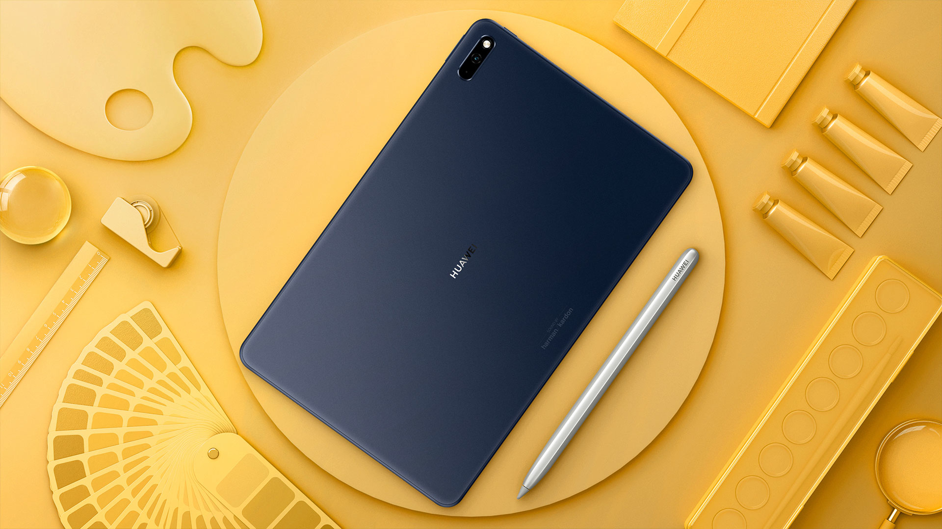 Draufsicht auf ein Huawei-Tablet, einen Stift und Kunstbedarf, die auf einer gelben Oberfläche angeordnet sind.