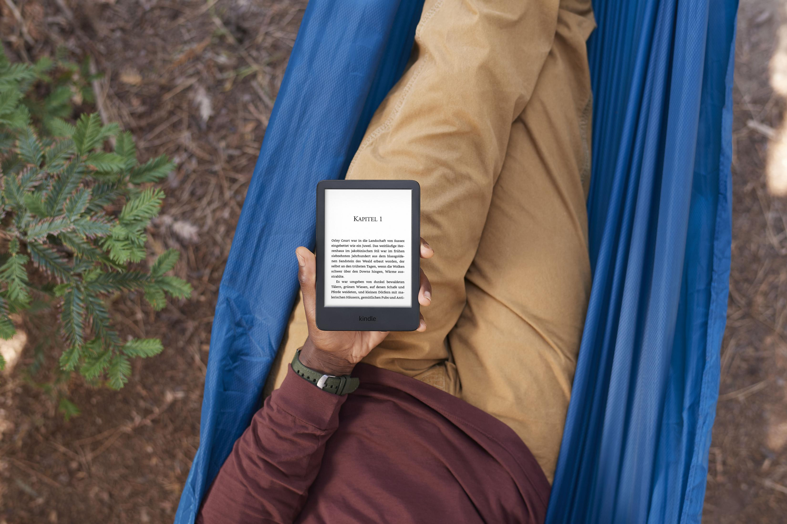 Eine Person liegt in einer Hängematte und liest einen E-Reader. Die Person trägt ein braunes Hemd und eine Hose.