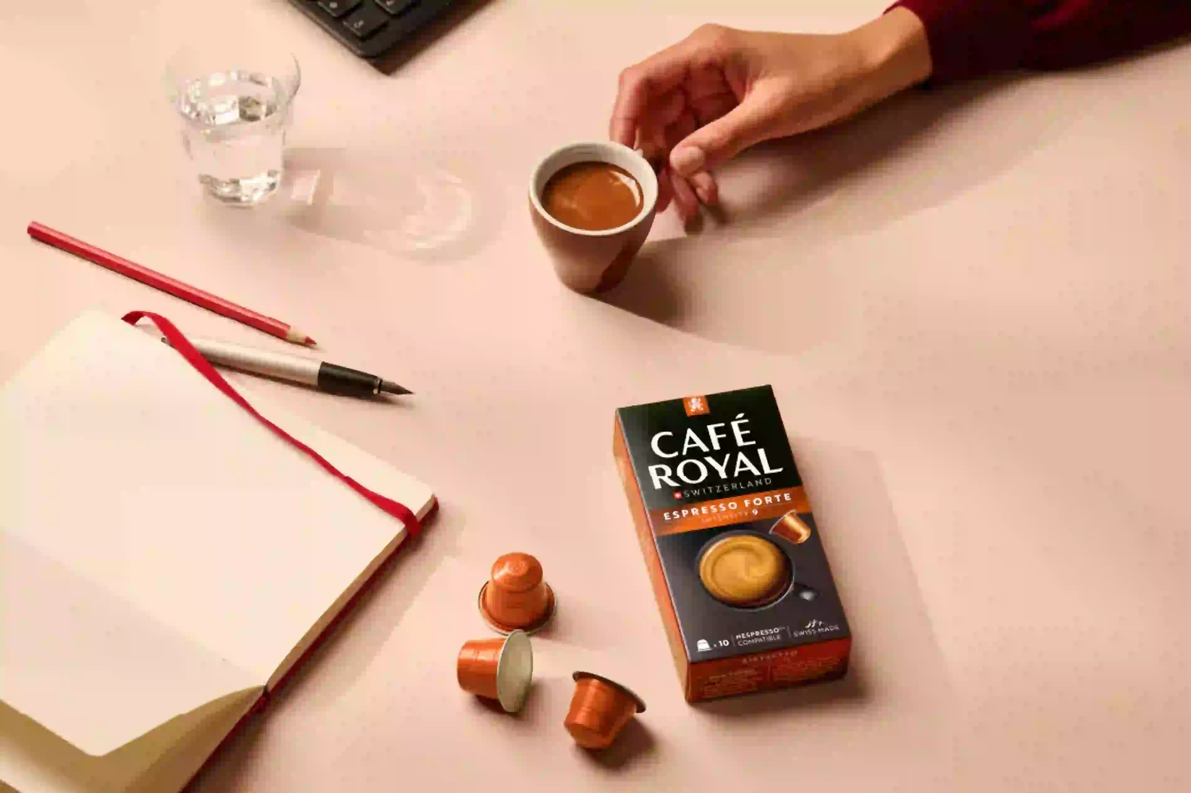 Ein Schreibtisch mit einer Kaffeetasse, Kapseln, einem Notizbuch und einer Cafe Royal-Box.