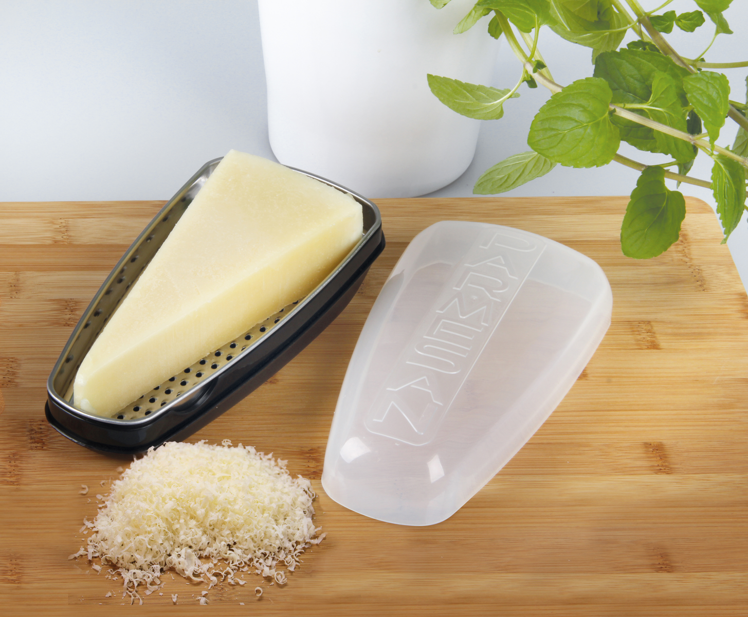 Parmesan und Reibe auf einem Holzschneidebrett neben einer Pflanze.