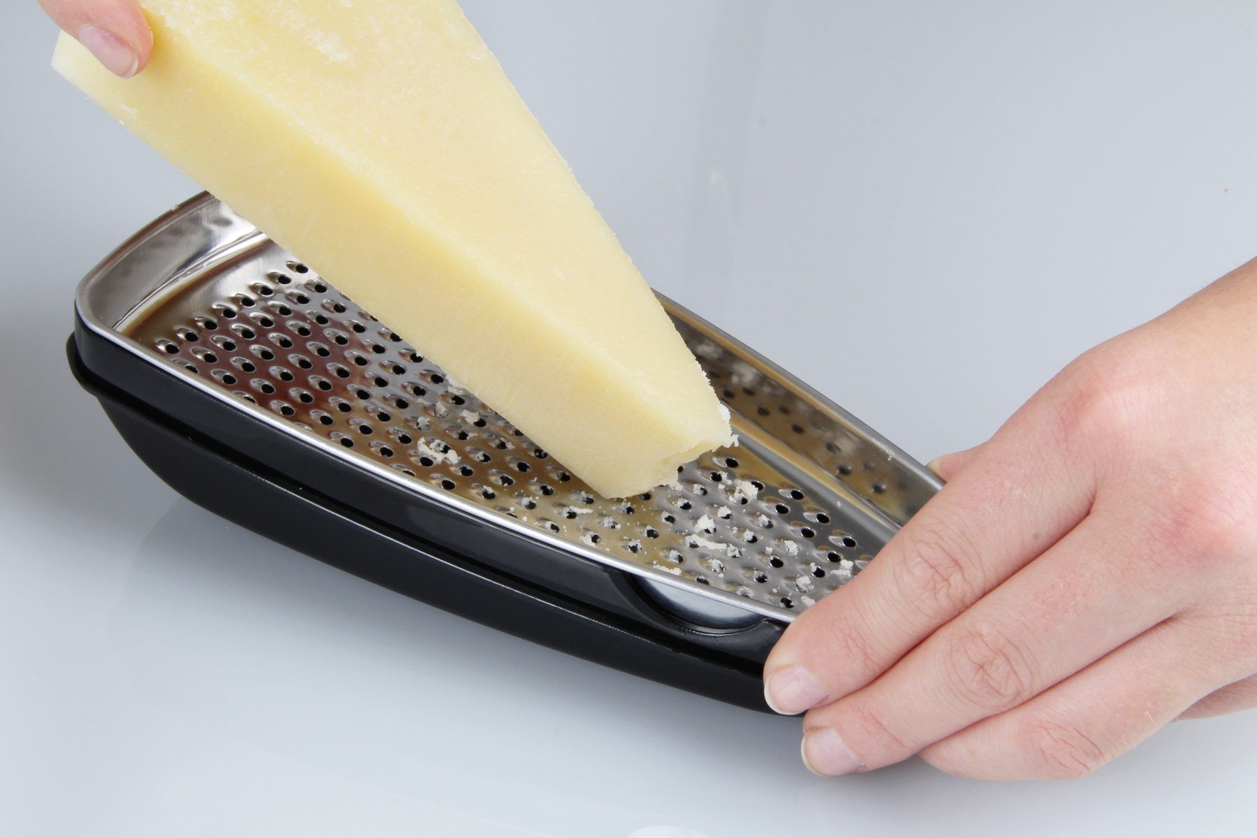 Eine Person reibt Parmesan mit einer schwarzen Reibe auf einem weißen Hintergrund.
