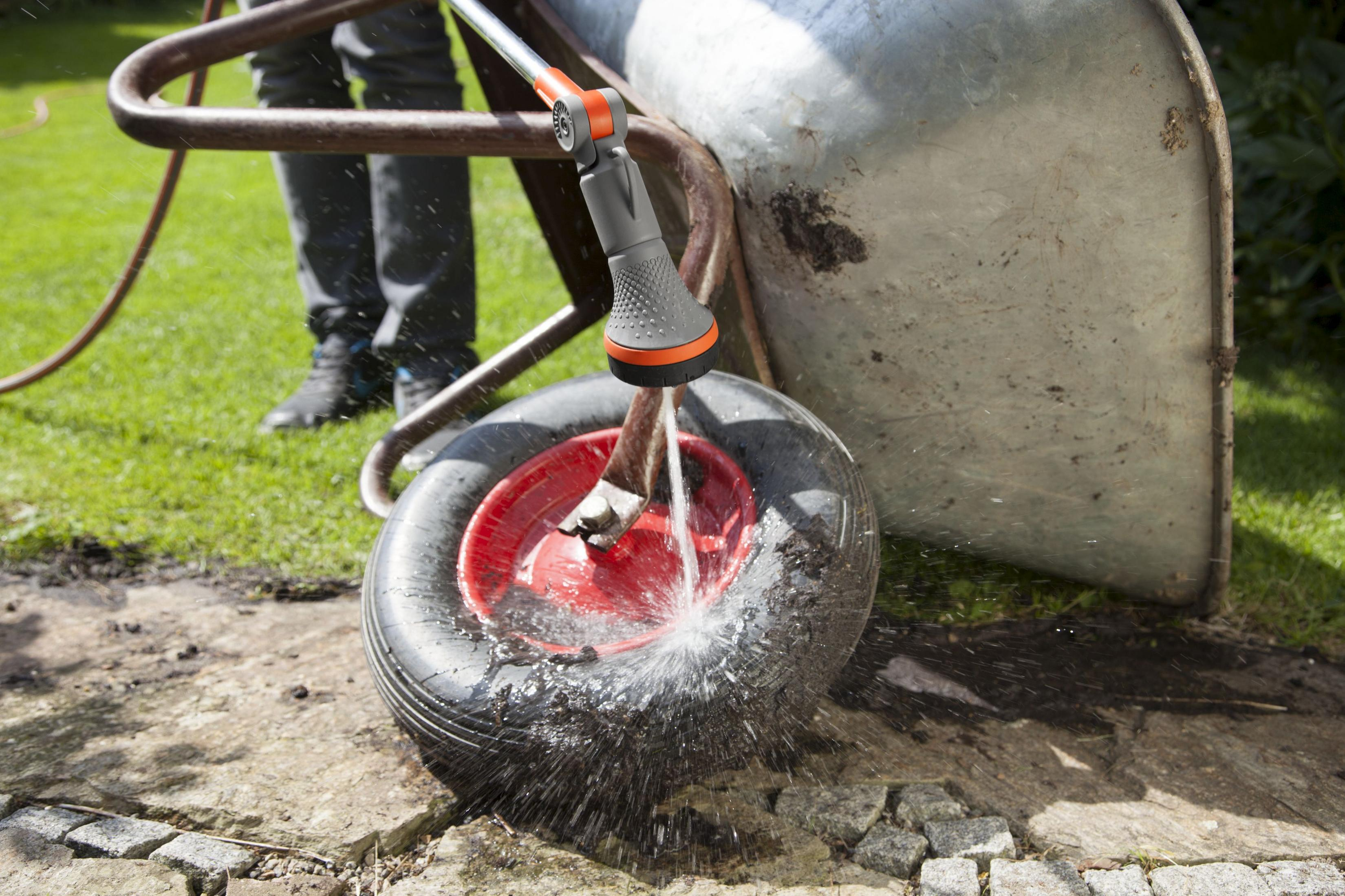 Una persona lava la ruota di una carriola con un tubo da giardino. L'acqua schizza sulla ruota.