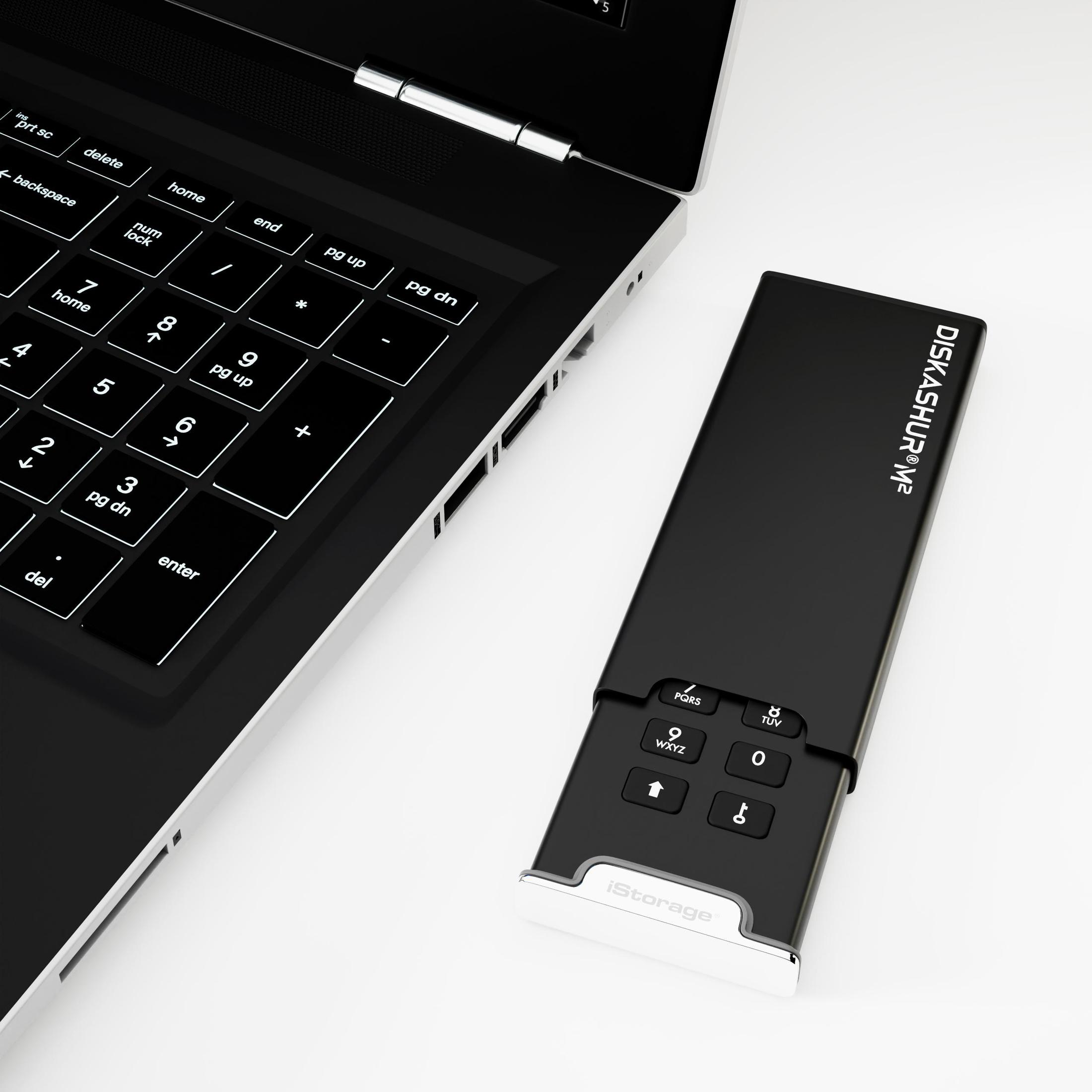 Eine schwarze Festplatte mit einer Tastatur neben einem Laptop auf einer weißen Oberfläche.
