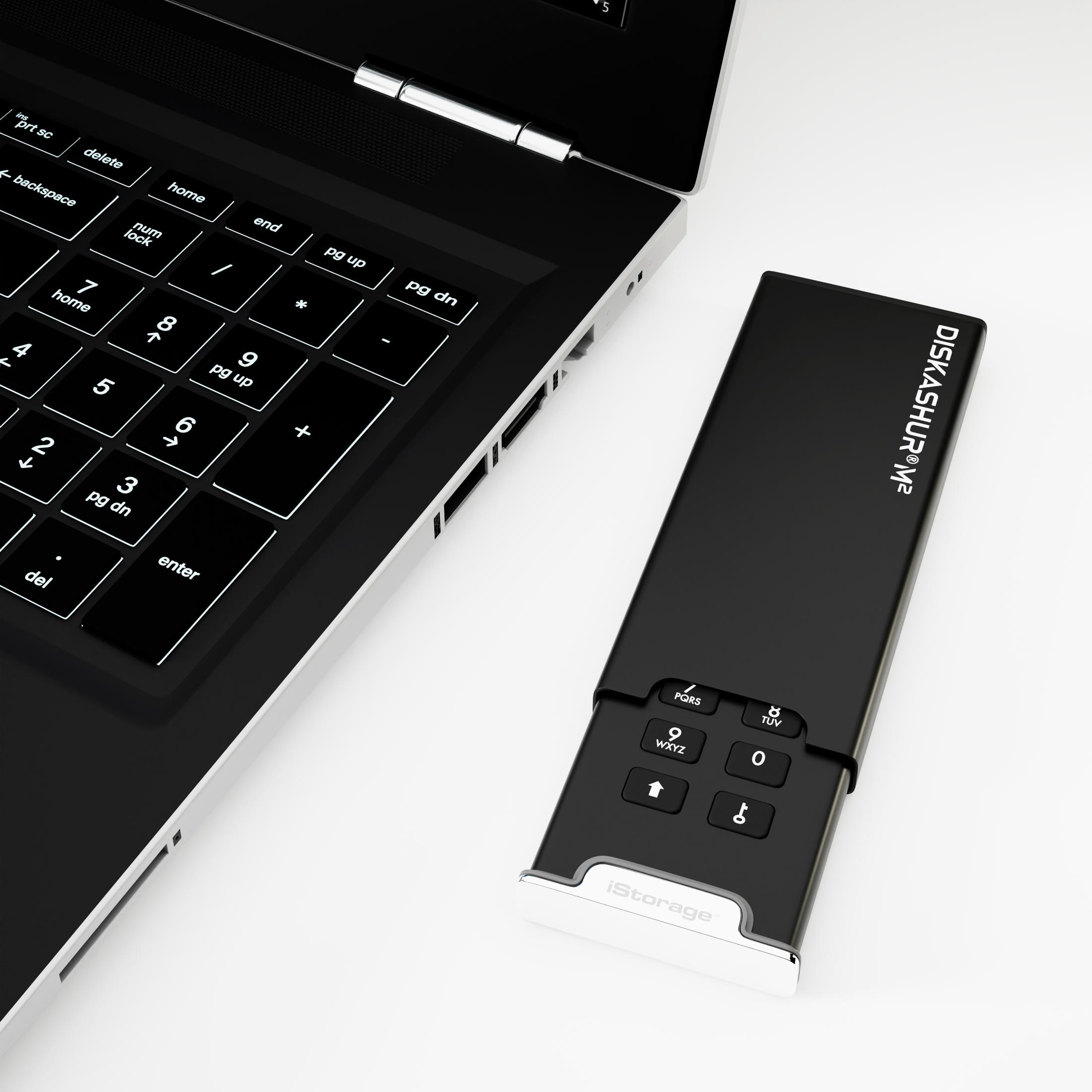 DISKASHUR M2 neben einem Laptop auf einer weißen Oberfläche.