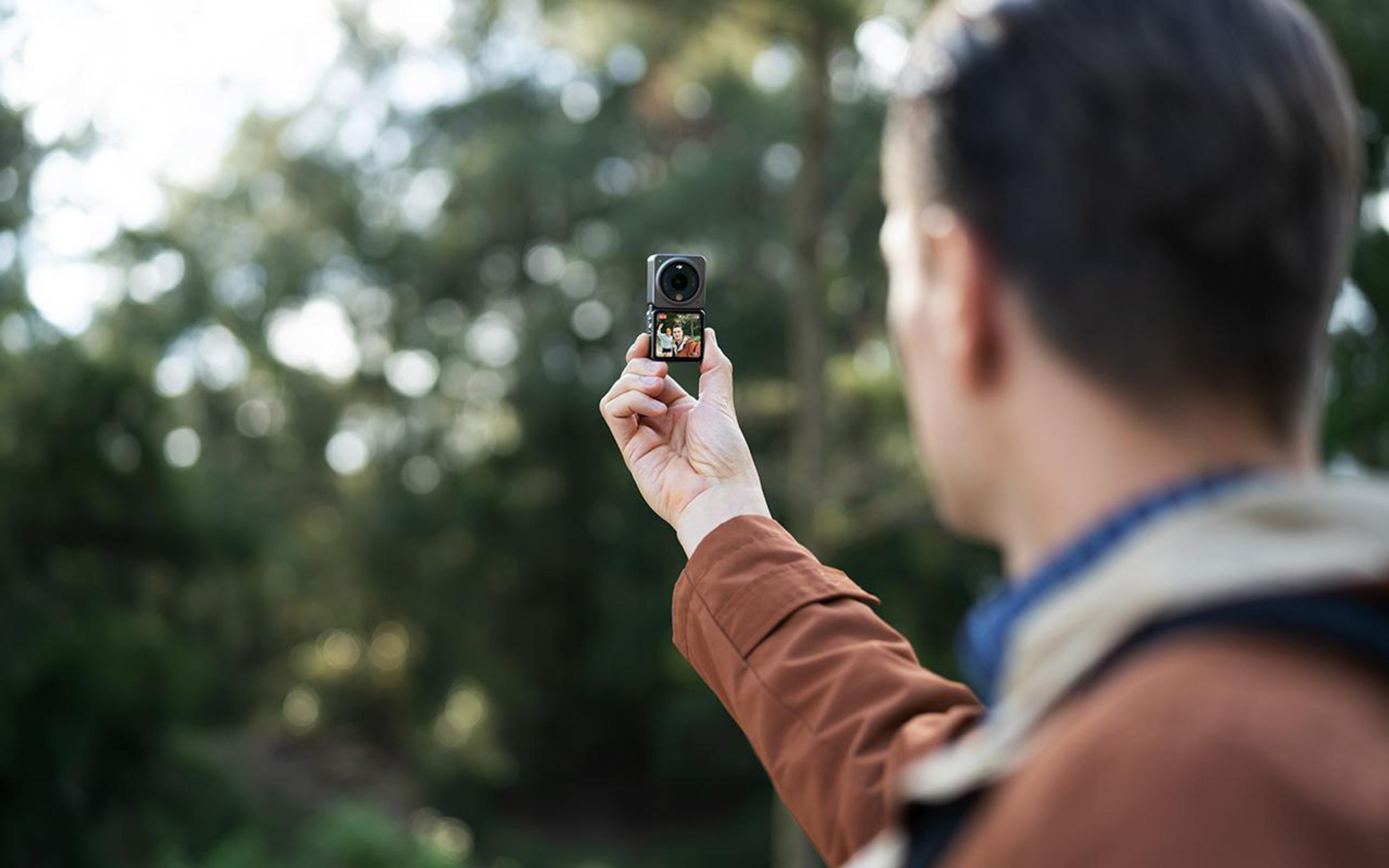 Una persona tiene una piccola fotocamera, mostrando uno schermo con un'immagine, su uno sfondo verde sfocato.