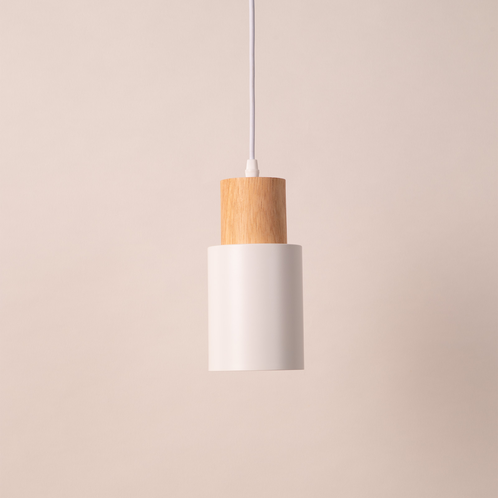 Lámpara colgante con una pantalla cilíndrica blanca y una parte superior de madera, que cuelga contra un fondo rosa pálido.