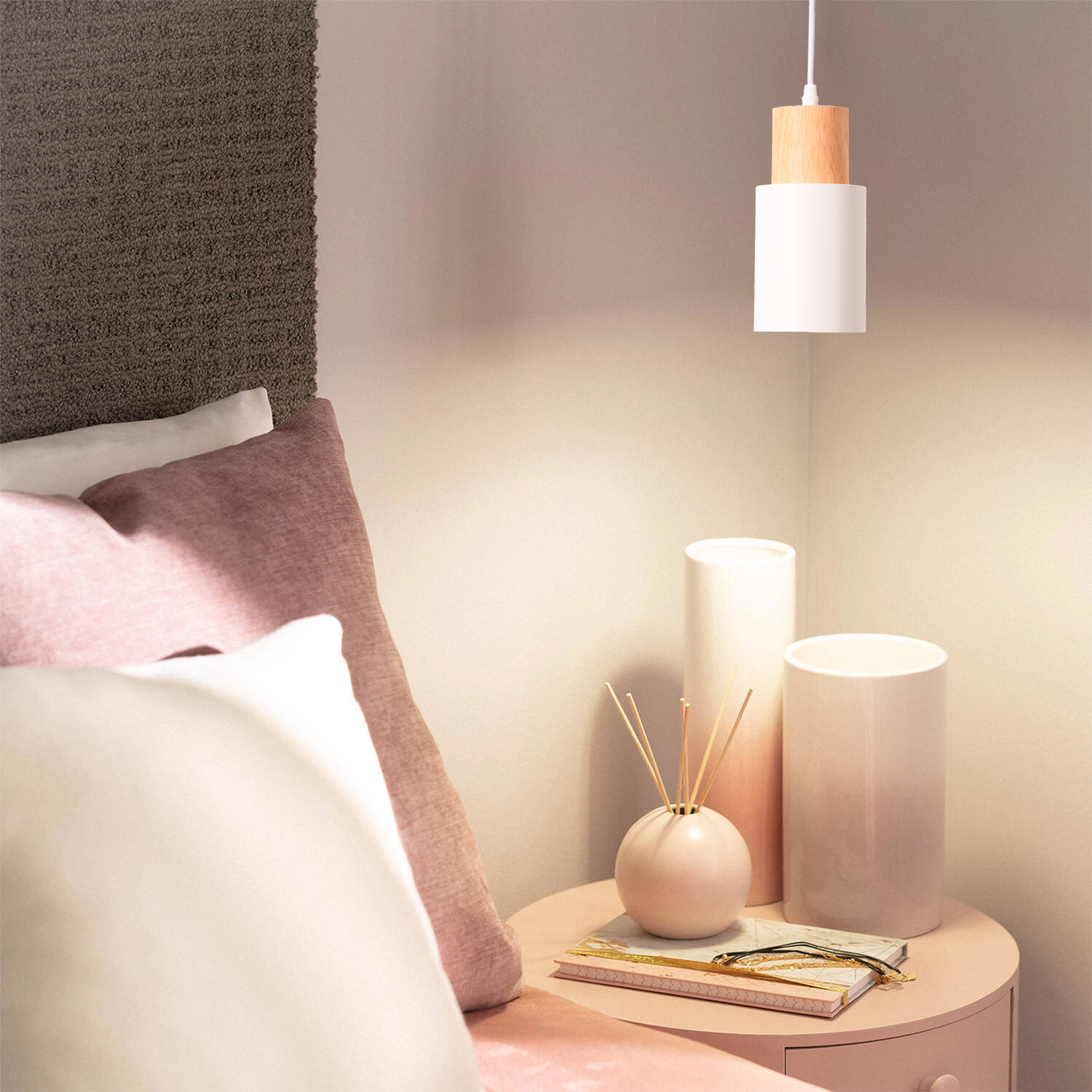 Una mesita de noche con una lámpara colgante blanca y de madera colgando encima en un acogedor dormitorio.