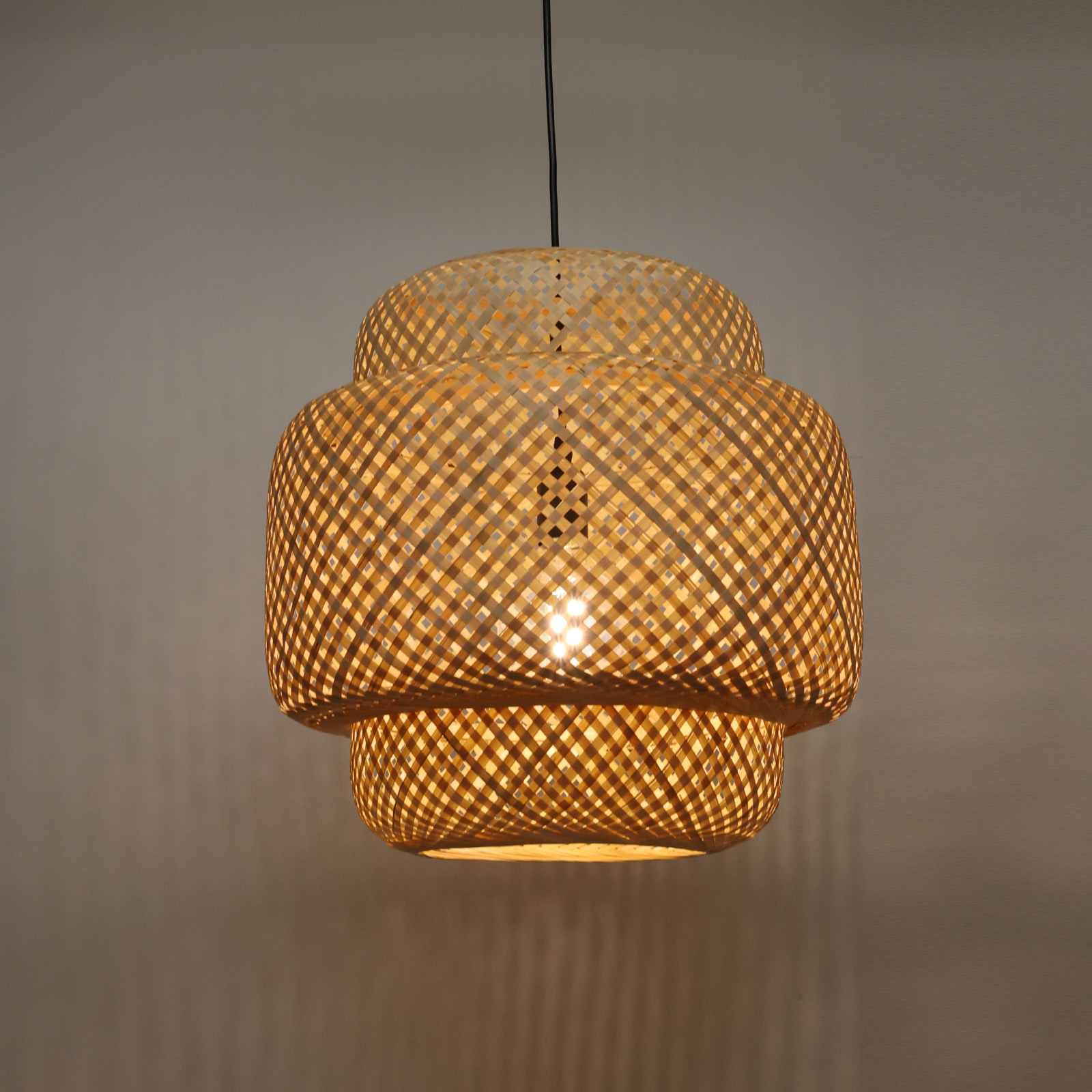 Una lámpara colgante de bambú tejido e iluminada cuelga contra una pared neutral, proyectando un brillo cálido.