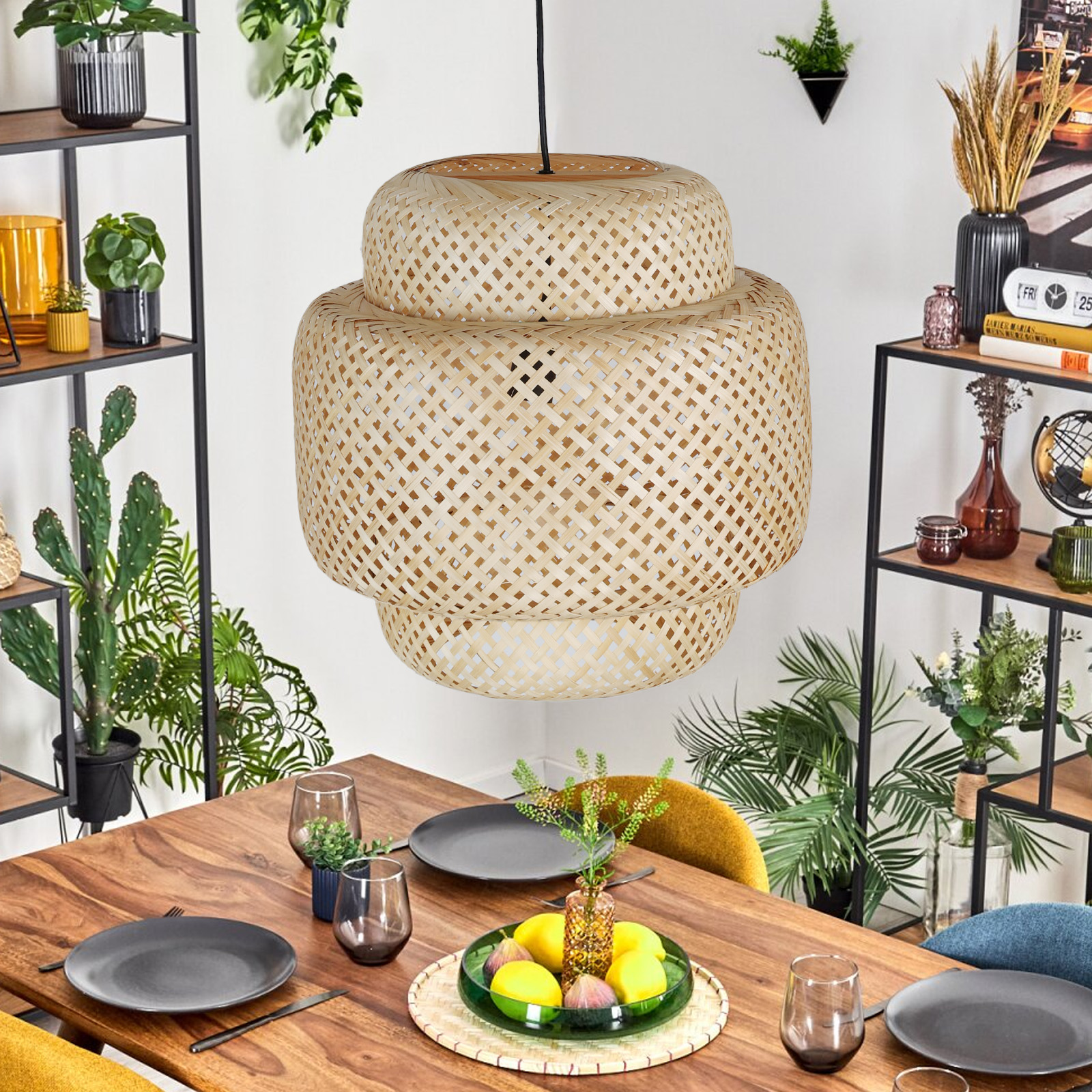Una lámpara colgante de bambú tejido cuelga sobre una mesa de comedor con platos y vasos, rodeada de plantas.
