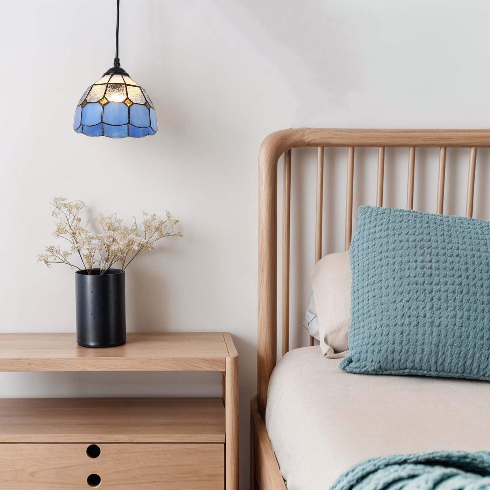 Escena de dormitorio con una lámpara colgante azul y blanca sobre una mesita de noche y cama de madera.
