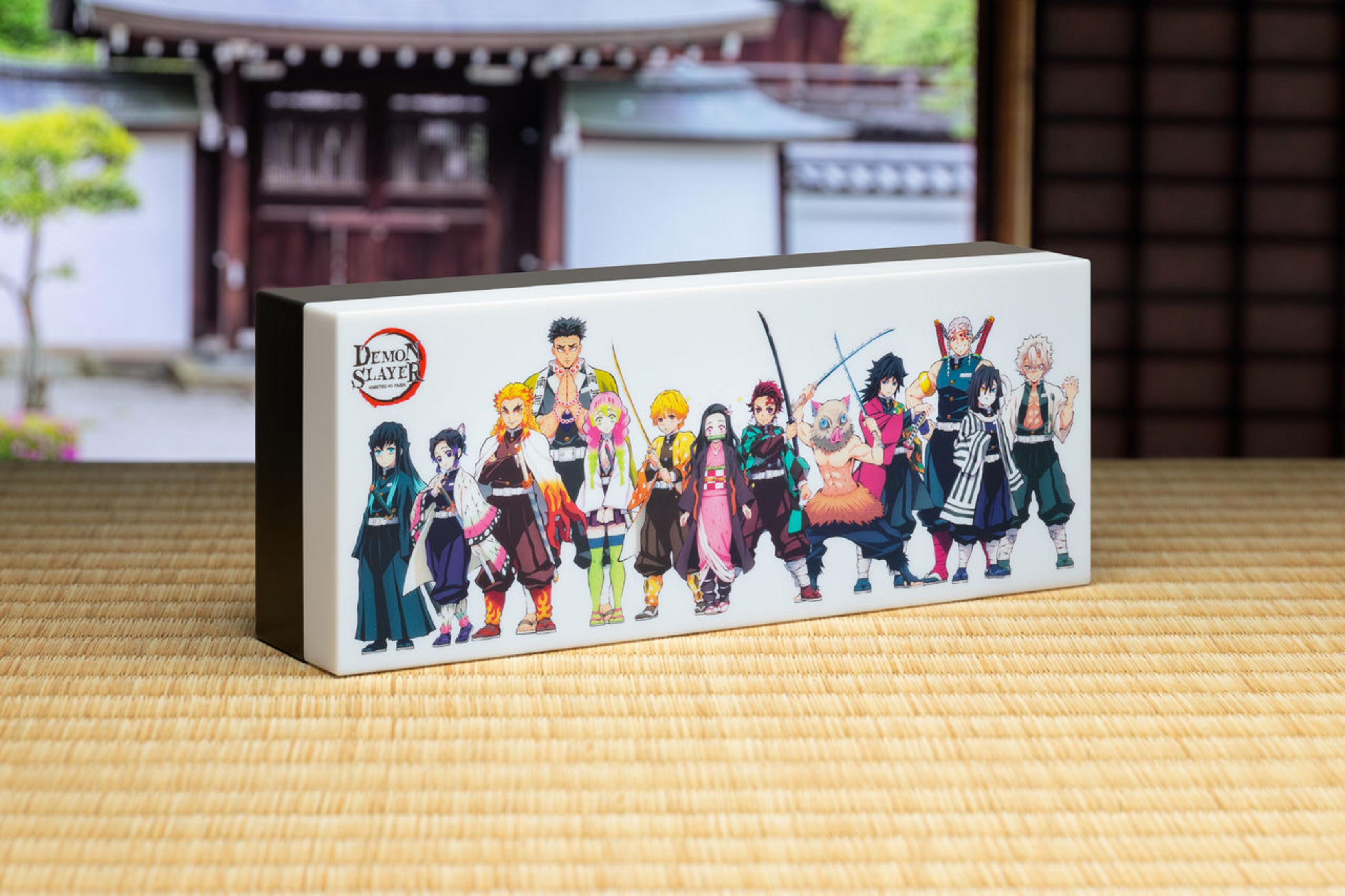 Eine Demon Slayer Leuchtbox auf einer Tatami-Matte, mit Anime-Charakteren und einem traditionellen japanischen Gebäude im Hintergrund.