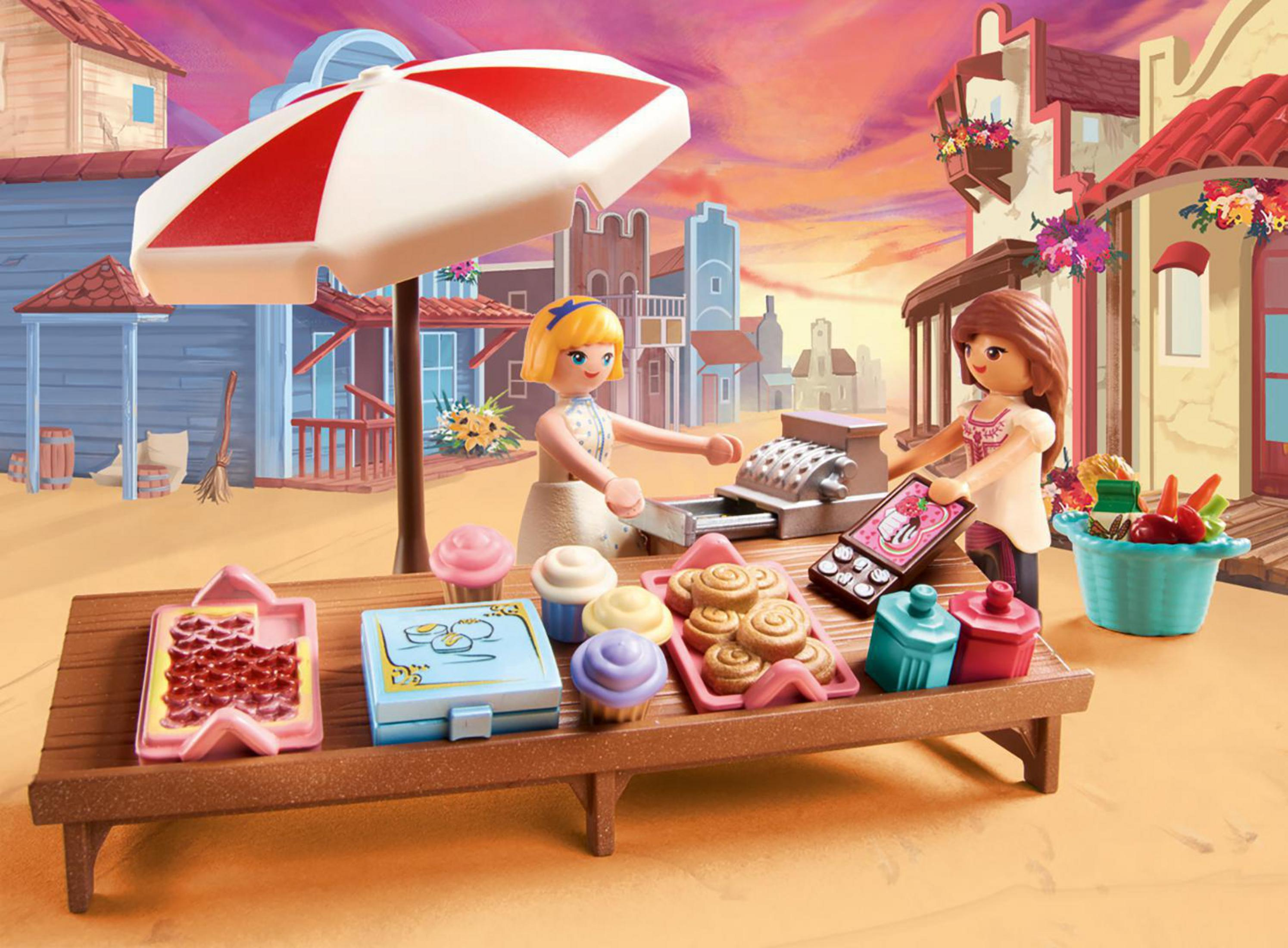 Escena de Playmobil de dos figuras en un puesto de mercado con pasteles y un paraguas rojo y blanco.