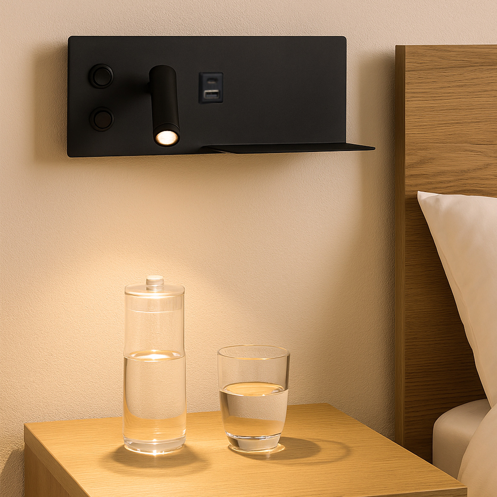 Una lámpara de pared negra con foco, puertos USB, estante, sobre una mesita de noche de madera, con una botella de agua y un vaso.