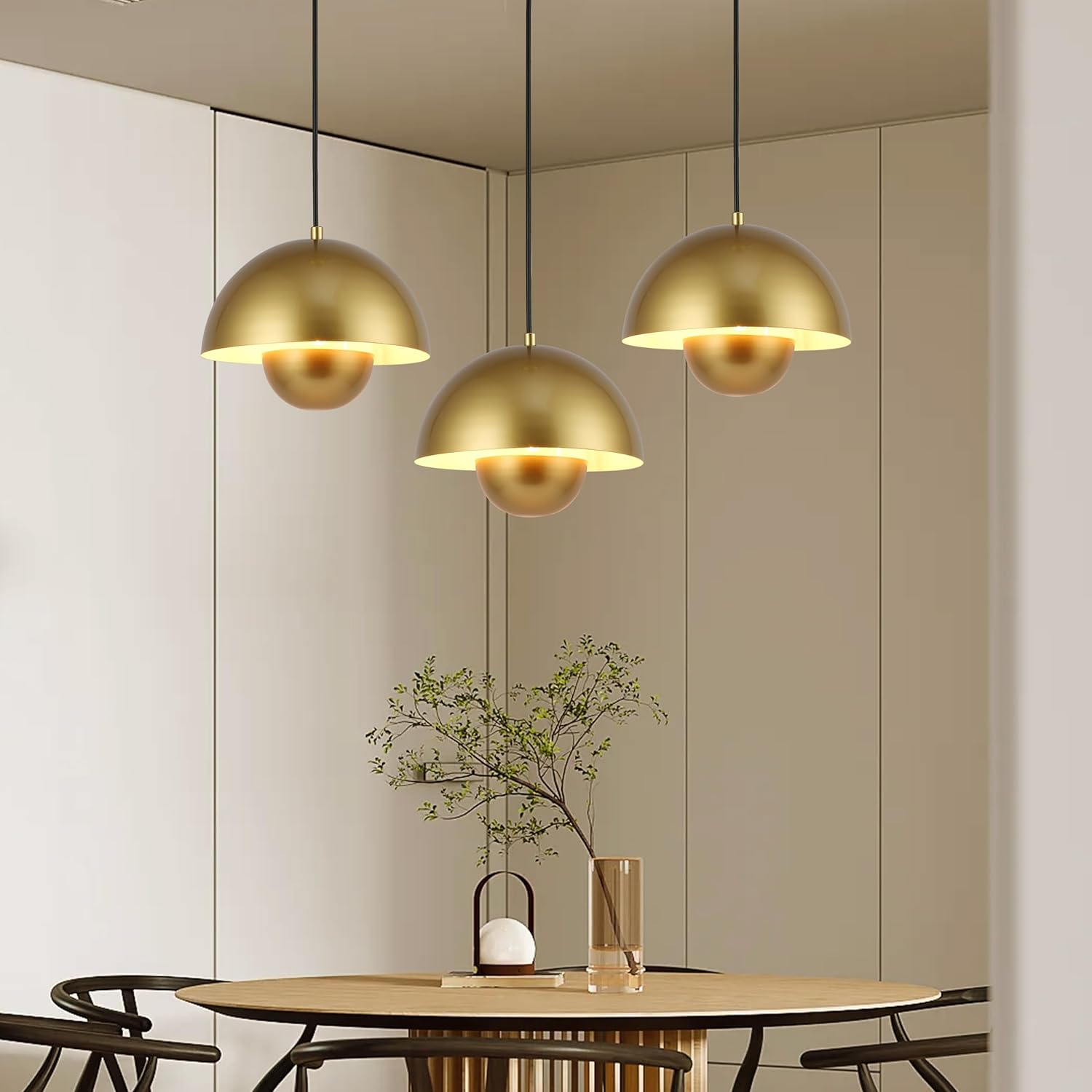 Tres lámparas colgantes doradas cuelgan sobre una mesa redonda de madera con sillas en un comedor luminoso.