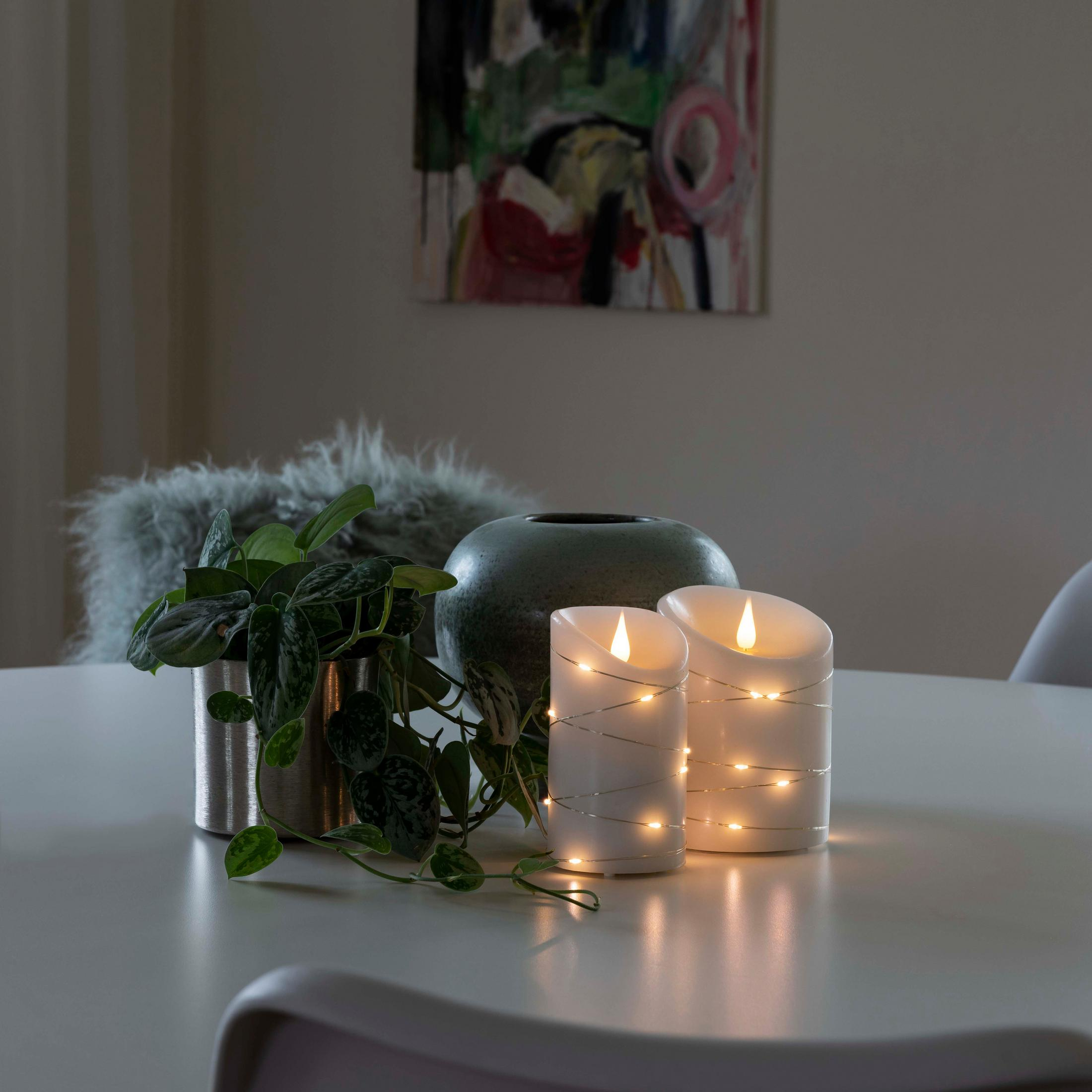 Kerzen auf einem Tisch mit einer Pflanze und Vase. Gemälde im Hintergrund.