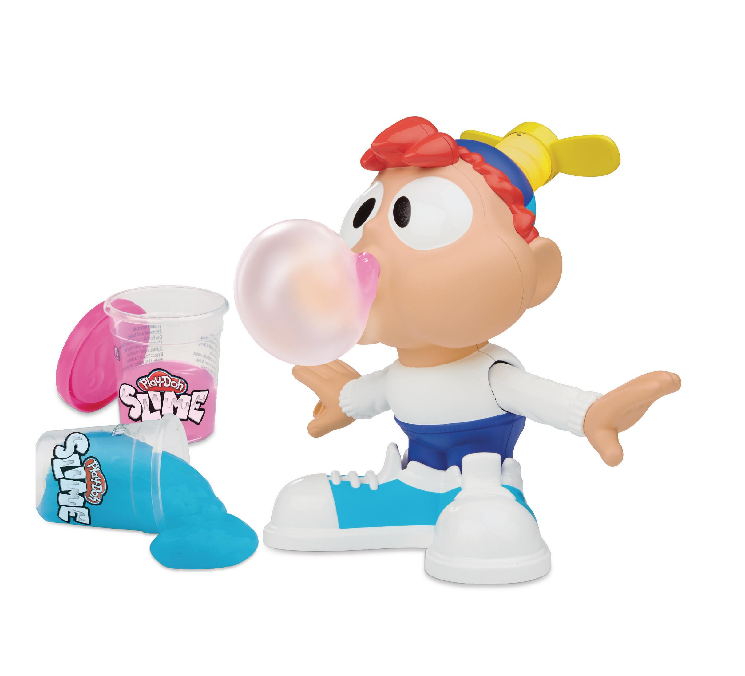 Spielzeugfigur, die eine Blase mit verschüttetem blauem Schleim bläst. Rosa Schleimbehälter und ein Lutscher auf einer weißen Oberfläche.