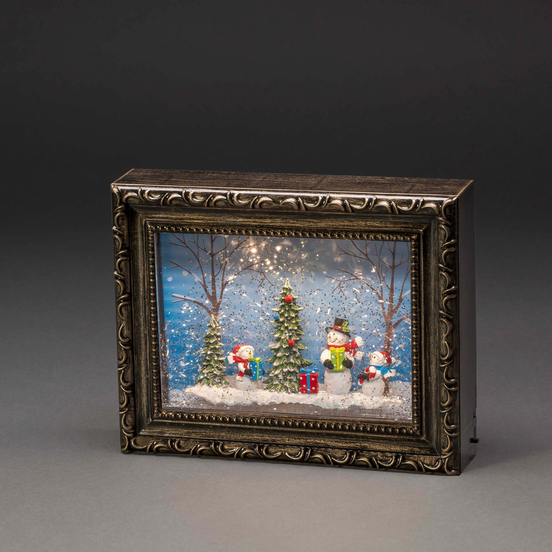 Gerahmte Schneekugel mit Schneemännern, Weihnachtsbäumen und Schnee auf dunklem Hintergrund.