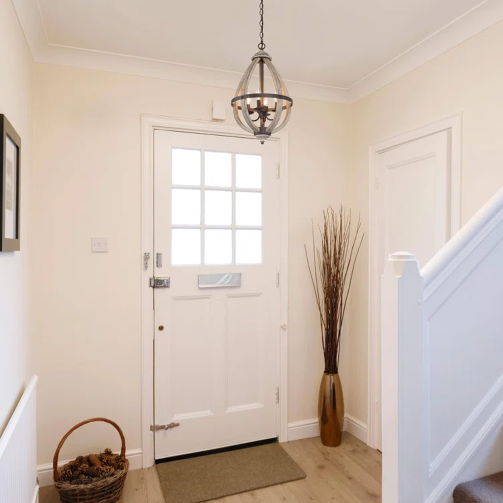 Entrada con candelabro de madera, puerta blanca, escaleras, canasta y jarrón con hierba alta.