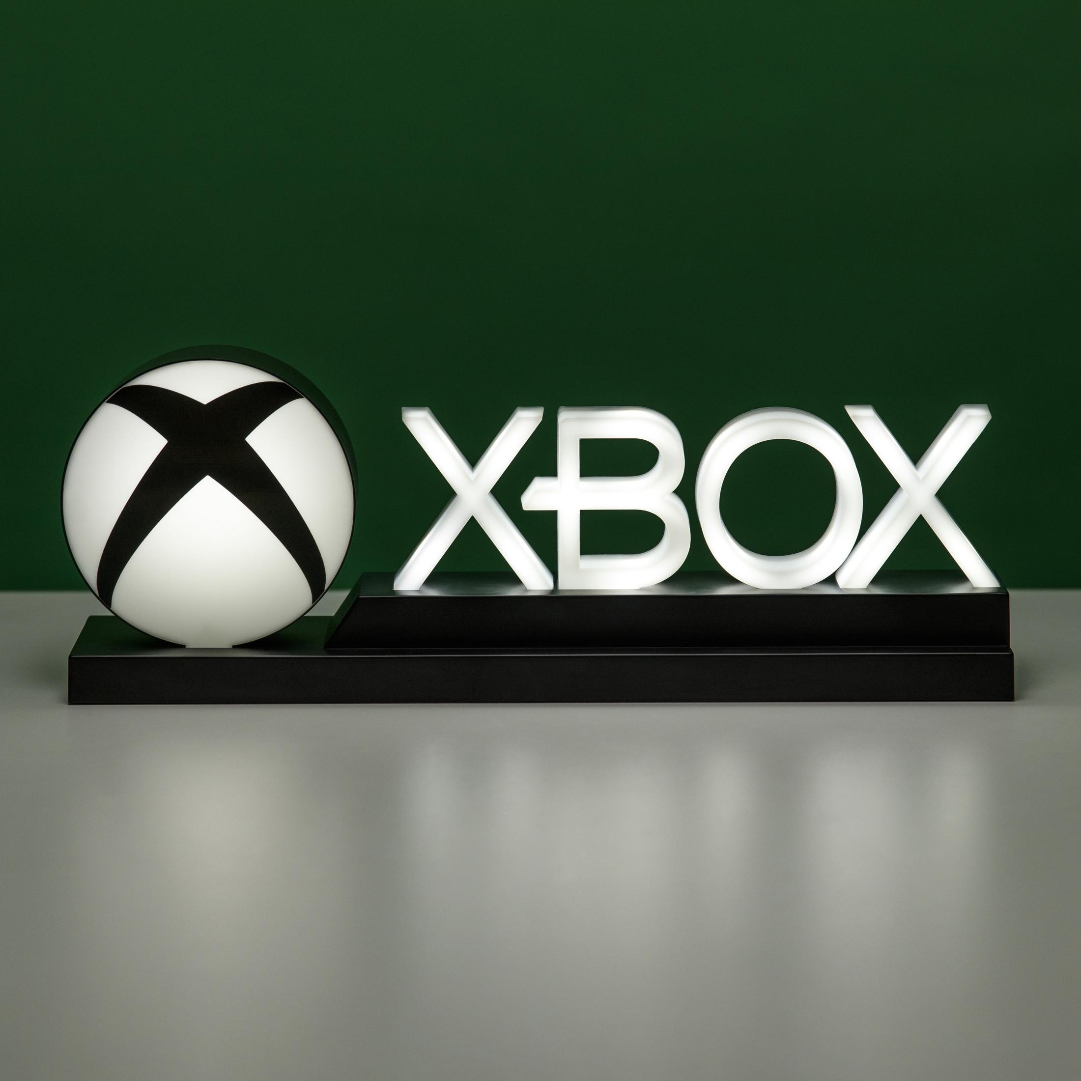 Ein Xbox-Licht mit dem Xbox-Logo auf einem schwarzen Ständer auf einer hellen Oberfläche mit grünem Hintergrund.
