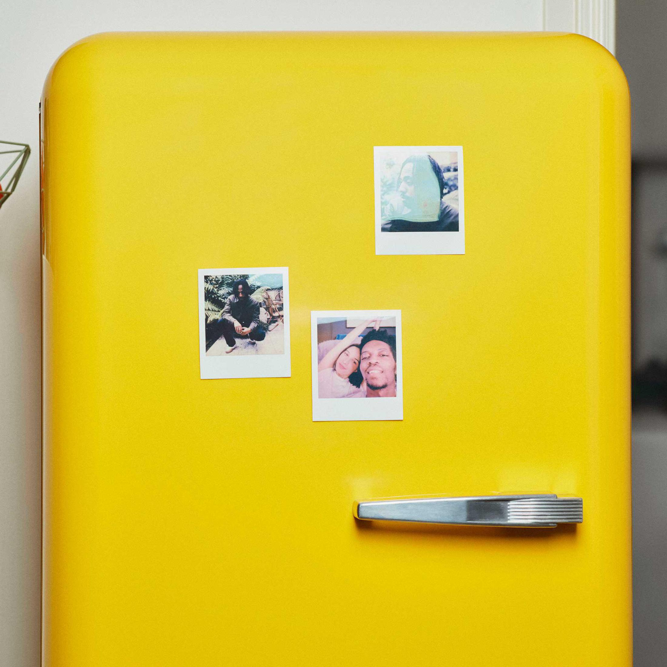 Un frigorifero giallo con foto istantanee attaccate alla porta.