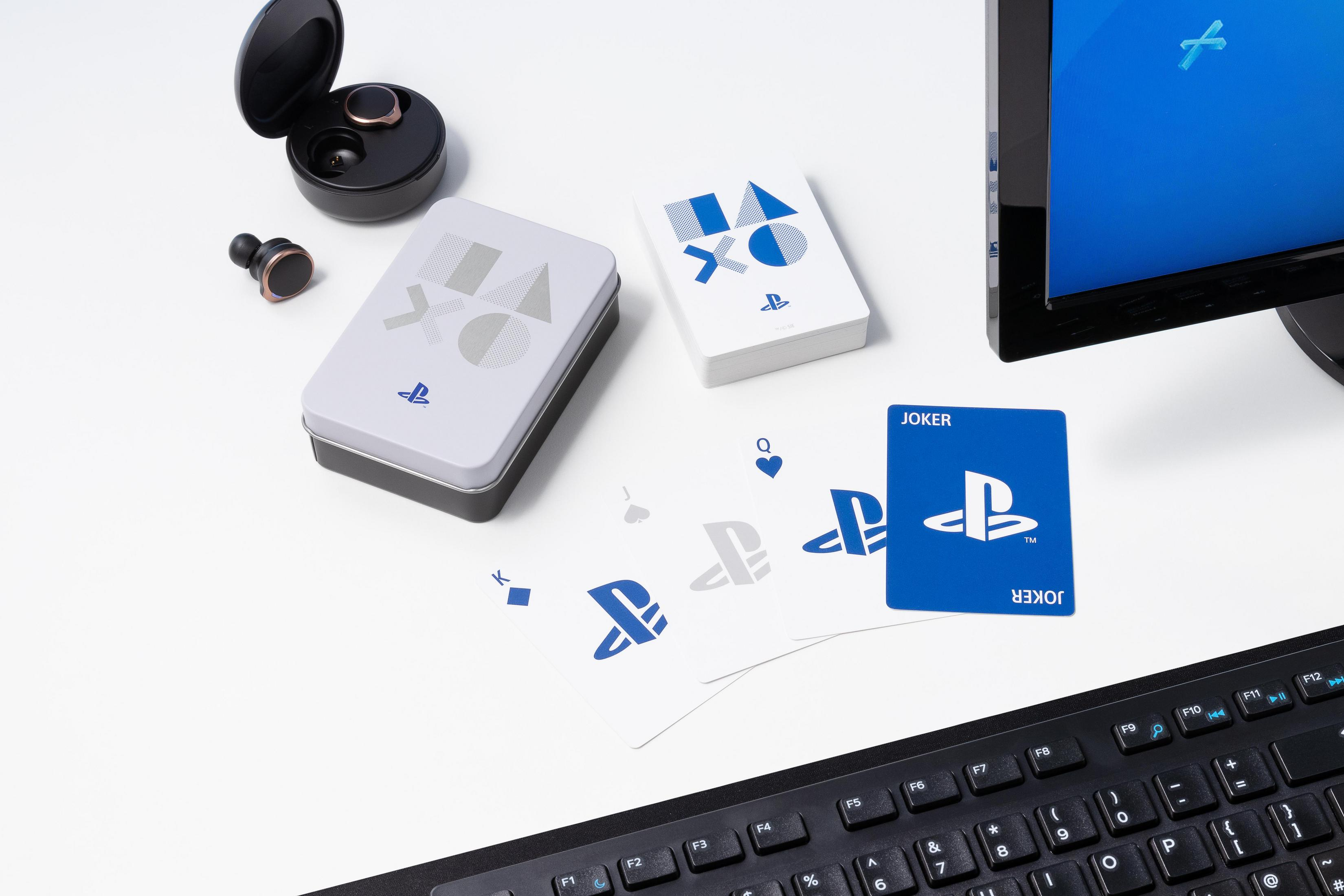 PlayStation-Karten mit einer Joker-Karte, kabellose Kopfhörer und eine Tastatur auf einem weißen Tisch.