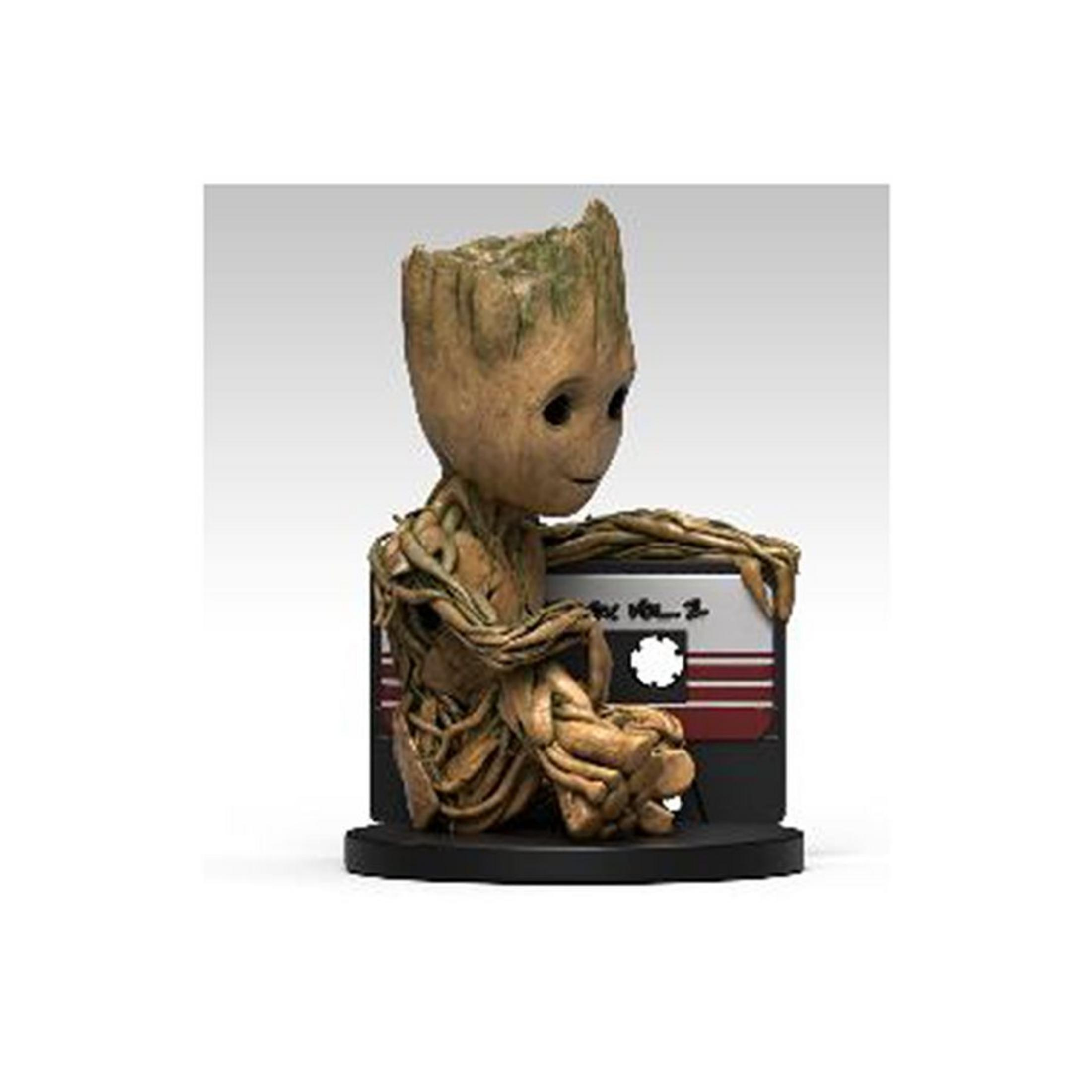Una figura de Groot sentado, sosteniendo una cinta de casete. Es marrón y de madera, con ojos grandes y una cara sonriente.