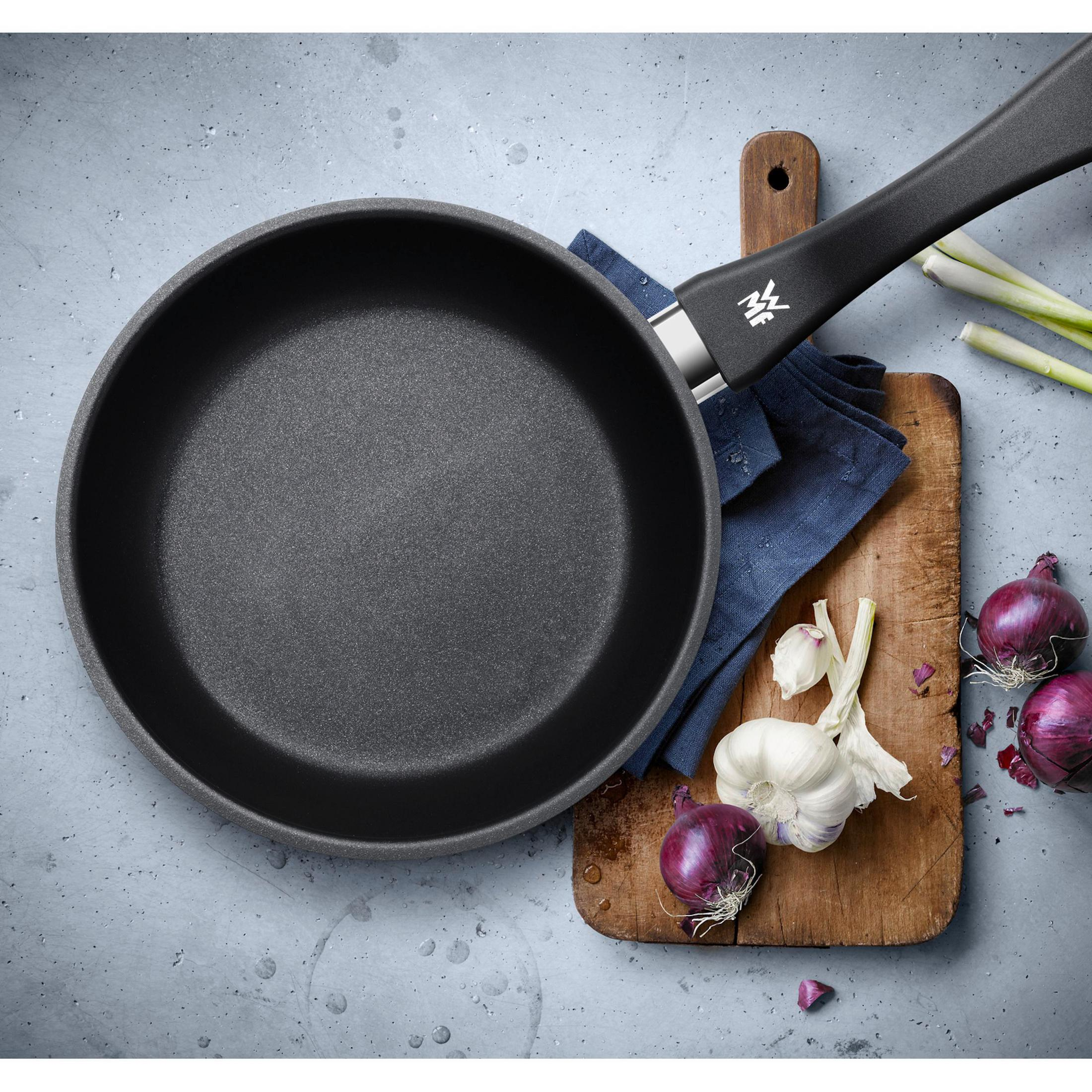 Poêle à frire noire avec des légumes sur une planche de bois et fond gris.