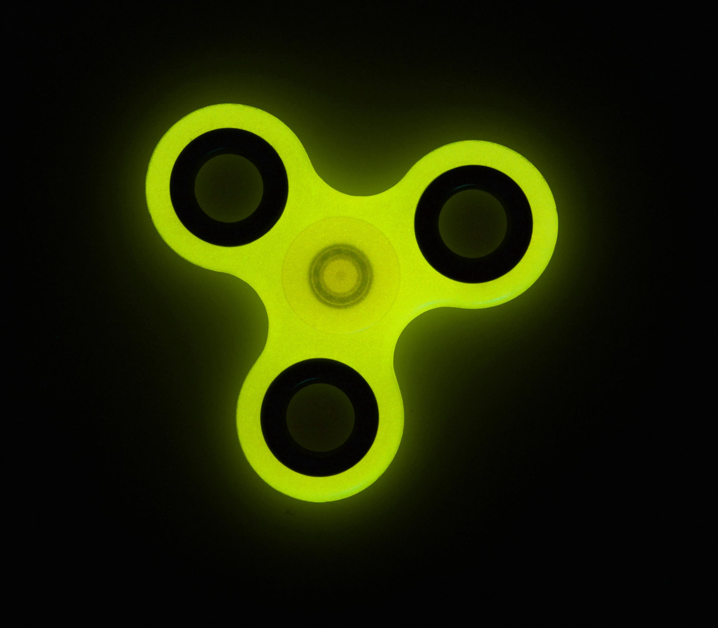 Ein grüner, im Dunkeln leuchtender Handspinner auf schwarzem Hintergrund.