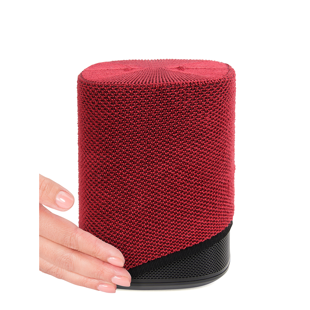 Un haut-parleur rouge avec un couvercle tissé est tenu par une main sur fond blanc.