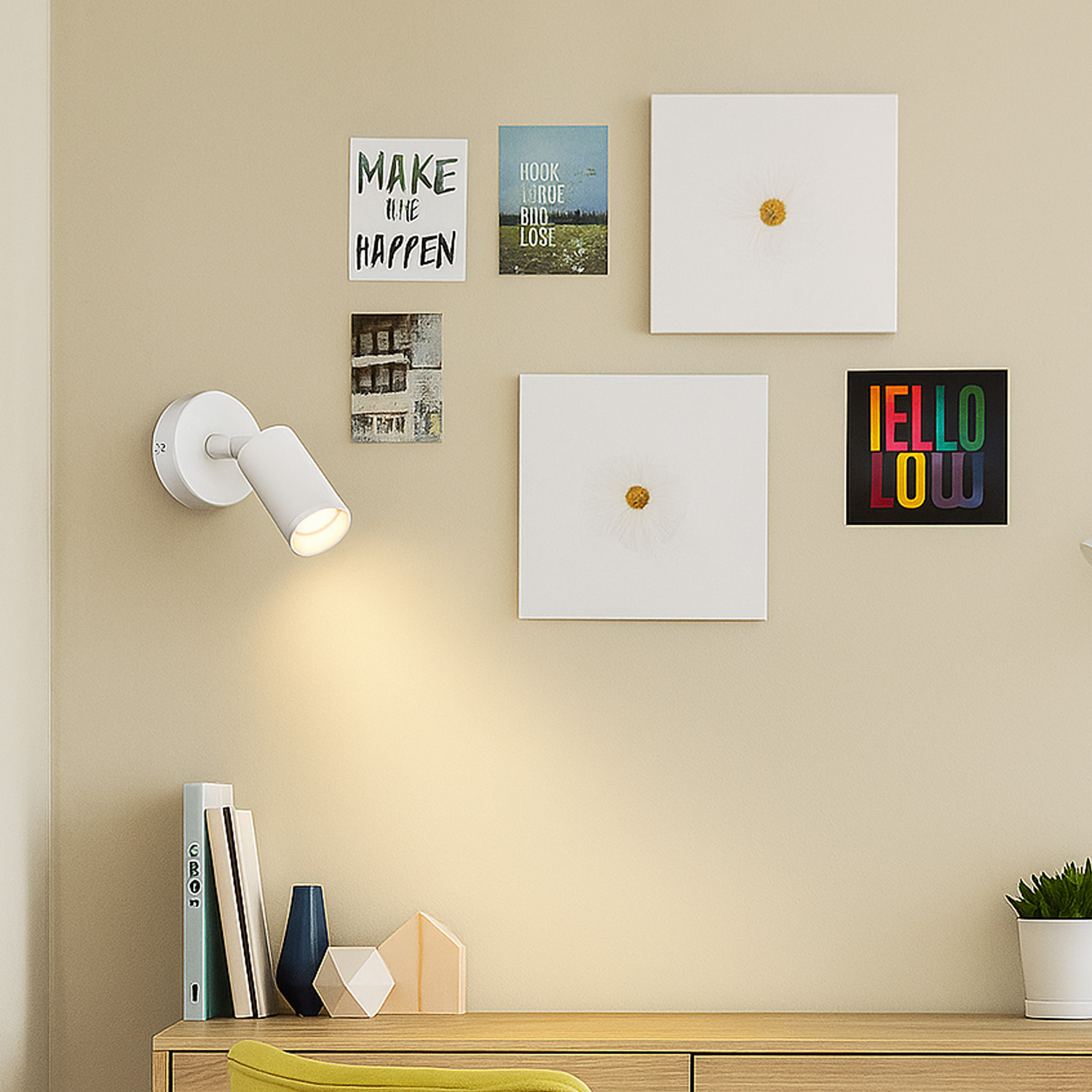 Lámpara de pared sobre escritorio con libros y arte. La lámpara es blanca y cilíndrica.