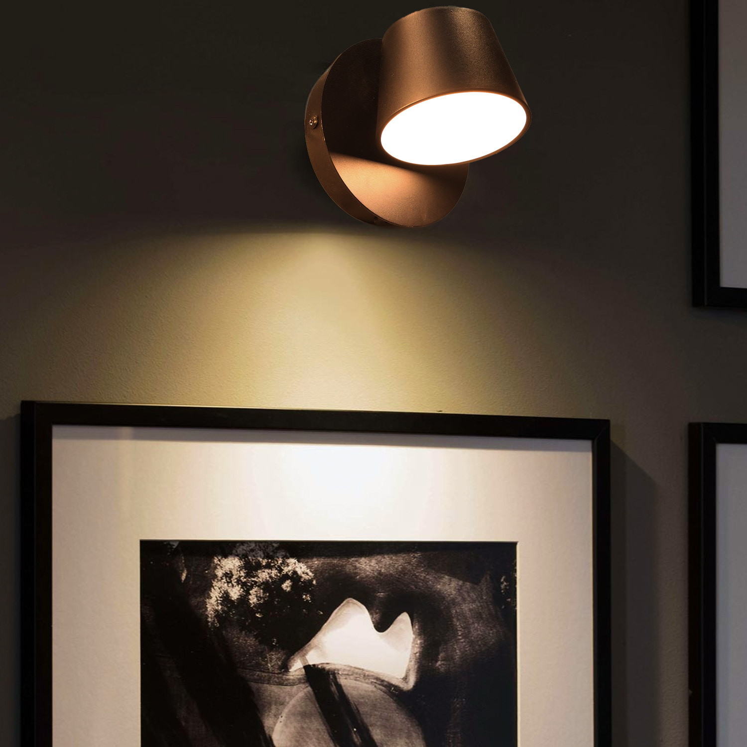 Una lámpara de pared de color bronce con una luz dirigida, montada sobre una obra de arte enmarcada.