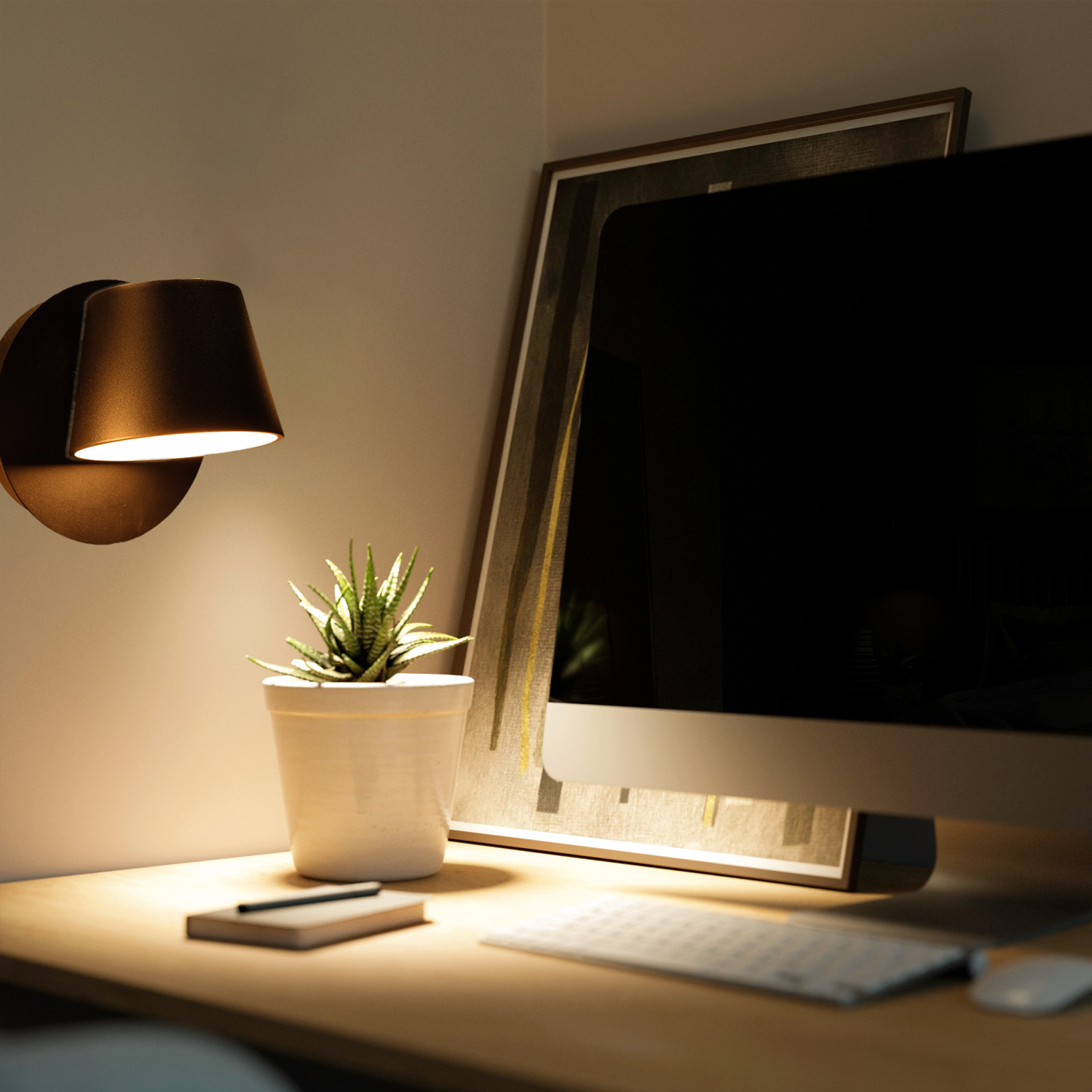 Configuración de escritorio con una lámpara negra, una planta en maceta, un monitor de computadora y un teclado, todo con luz suave.