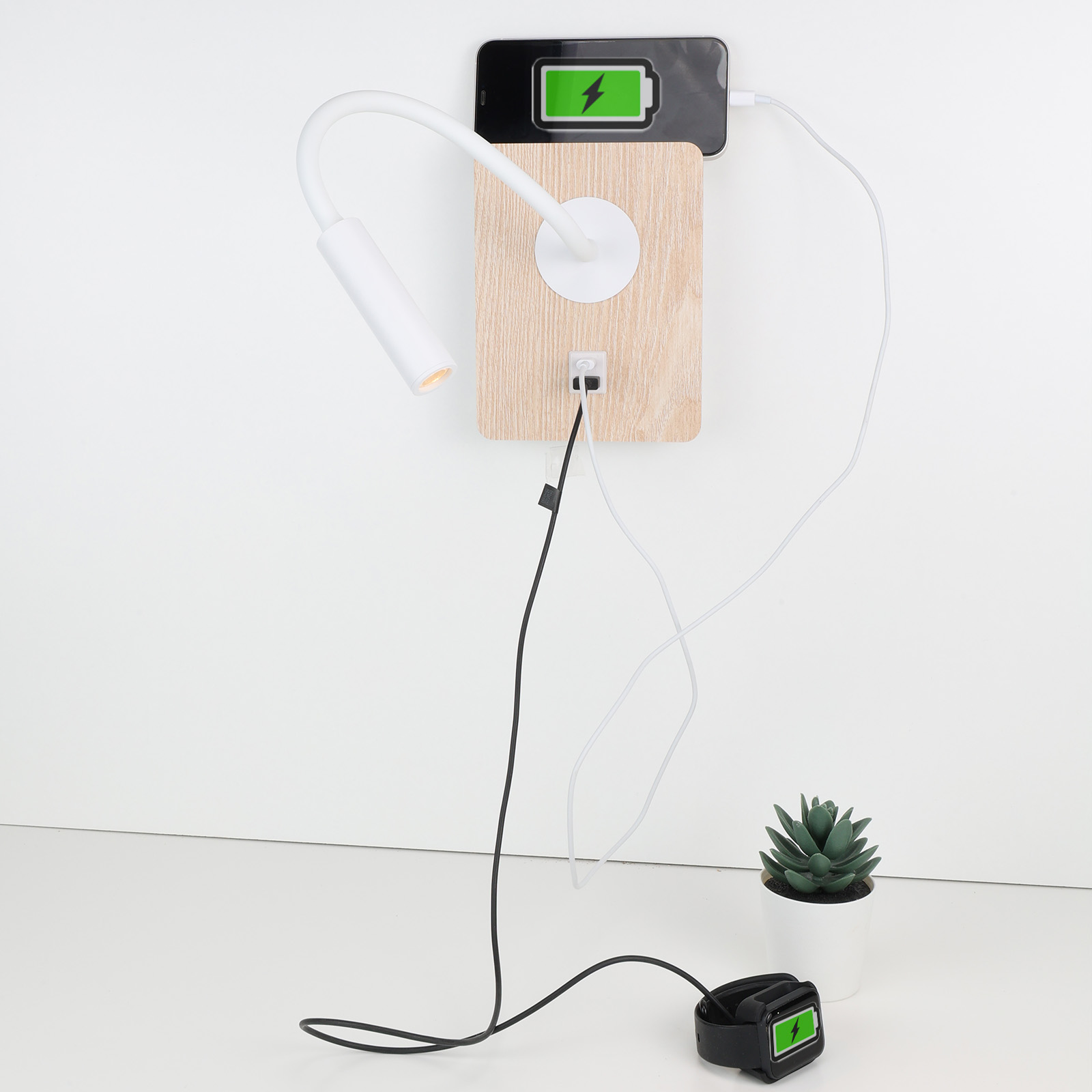 Una lámpara de pared con una estación de carga, mostrando un teléfono cargándose y una planta suculenta en un escritorio blanco.