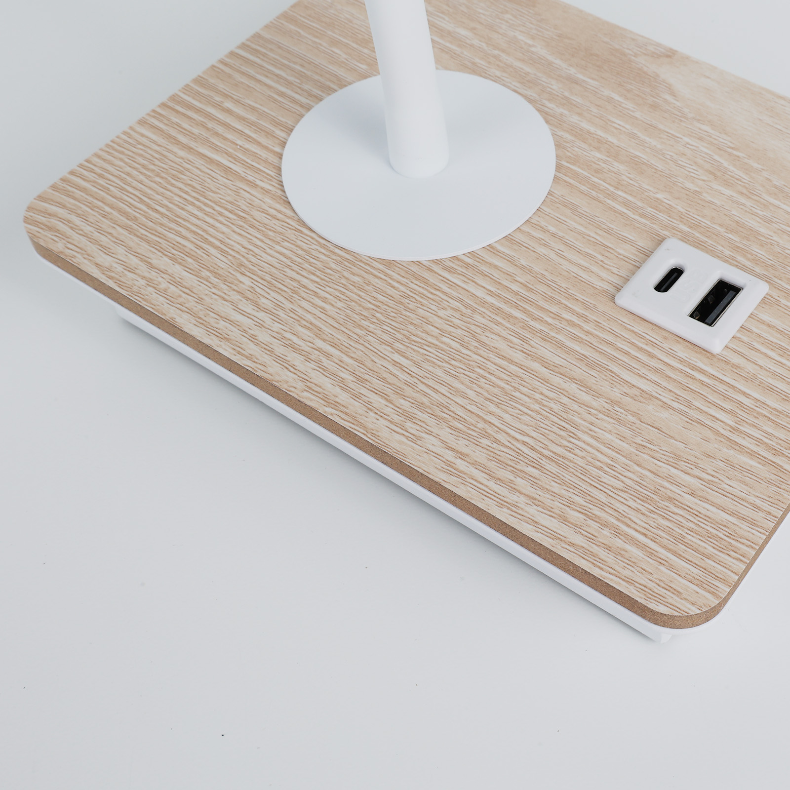 Un primer plano de una base de lámpara de madera con un vástago de lámpara blanco y puertos USB, sobre una superficie blanca.