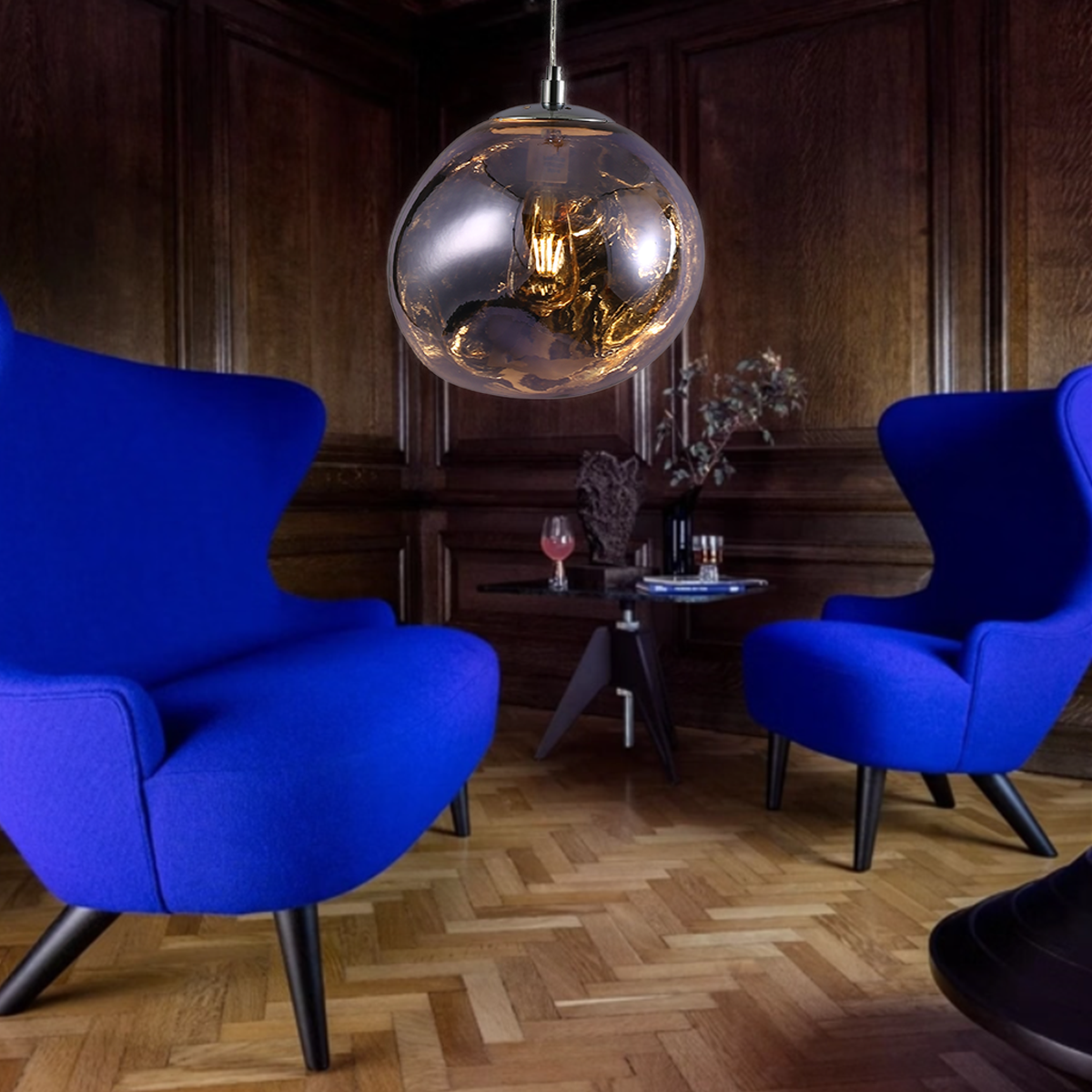 Una lámpara colgante de cristal moteado cuelga en una habitación con sillas azules y paneles de madera.