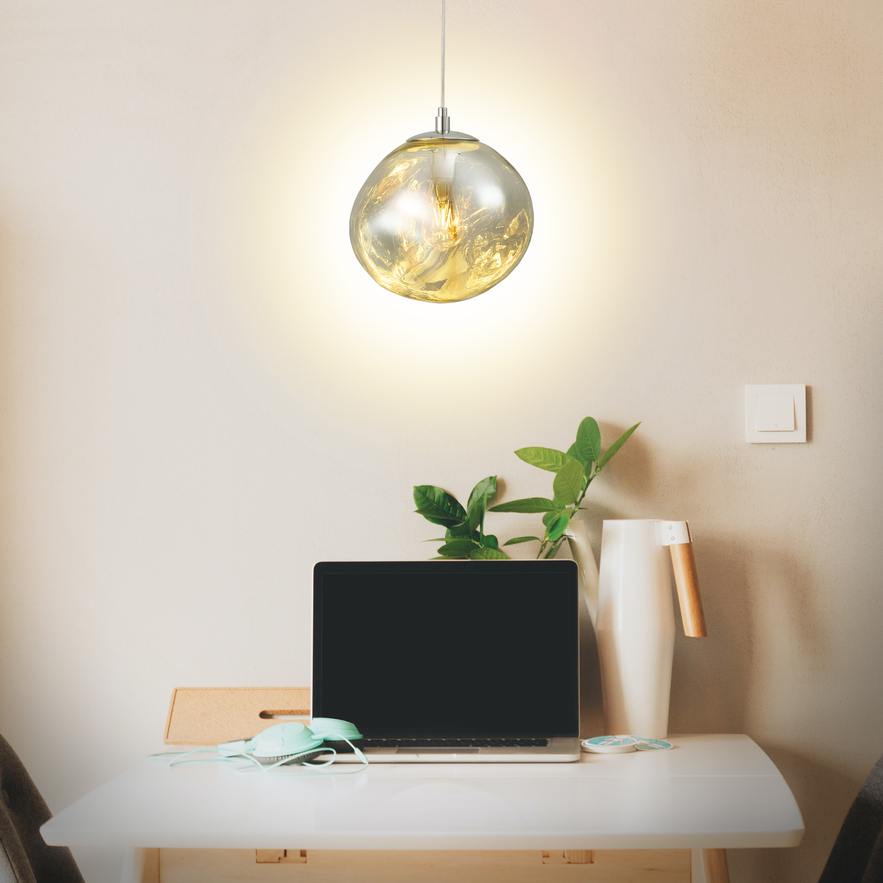 Lámpara colgante sobre un escritorio con un portátil, una planta y accesorios en una habitación.