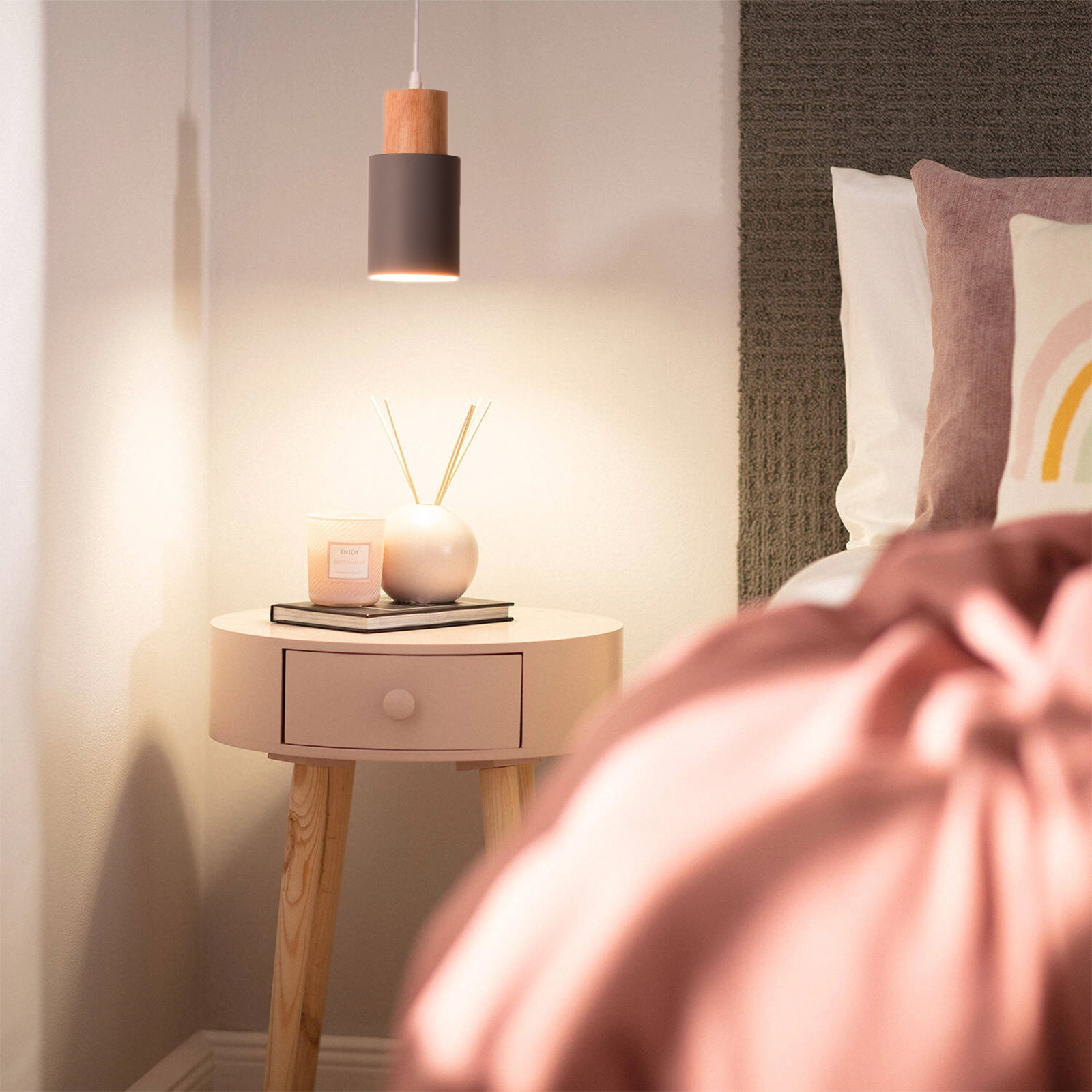 Una mesita de noche con una lámpara, vela y difusor junto a una cama con ropa de cama rosa.