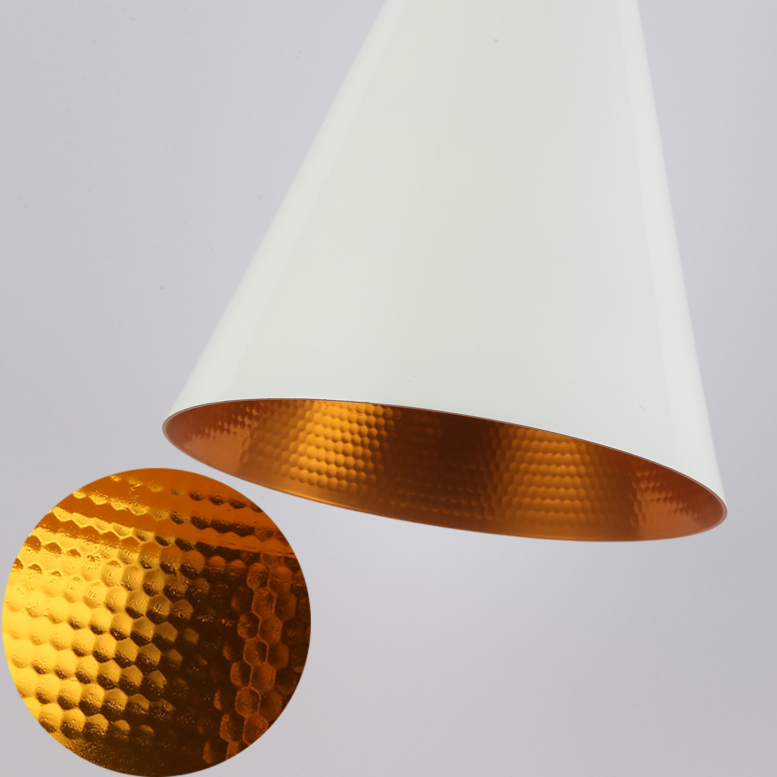 Un primer plano muestra una lámpara colgante blanca con un interior de oro martillado, resaltando la textura.