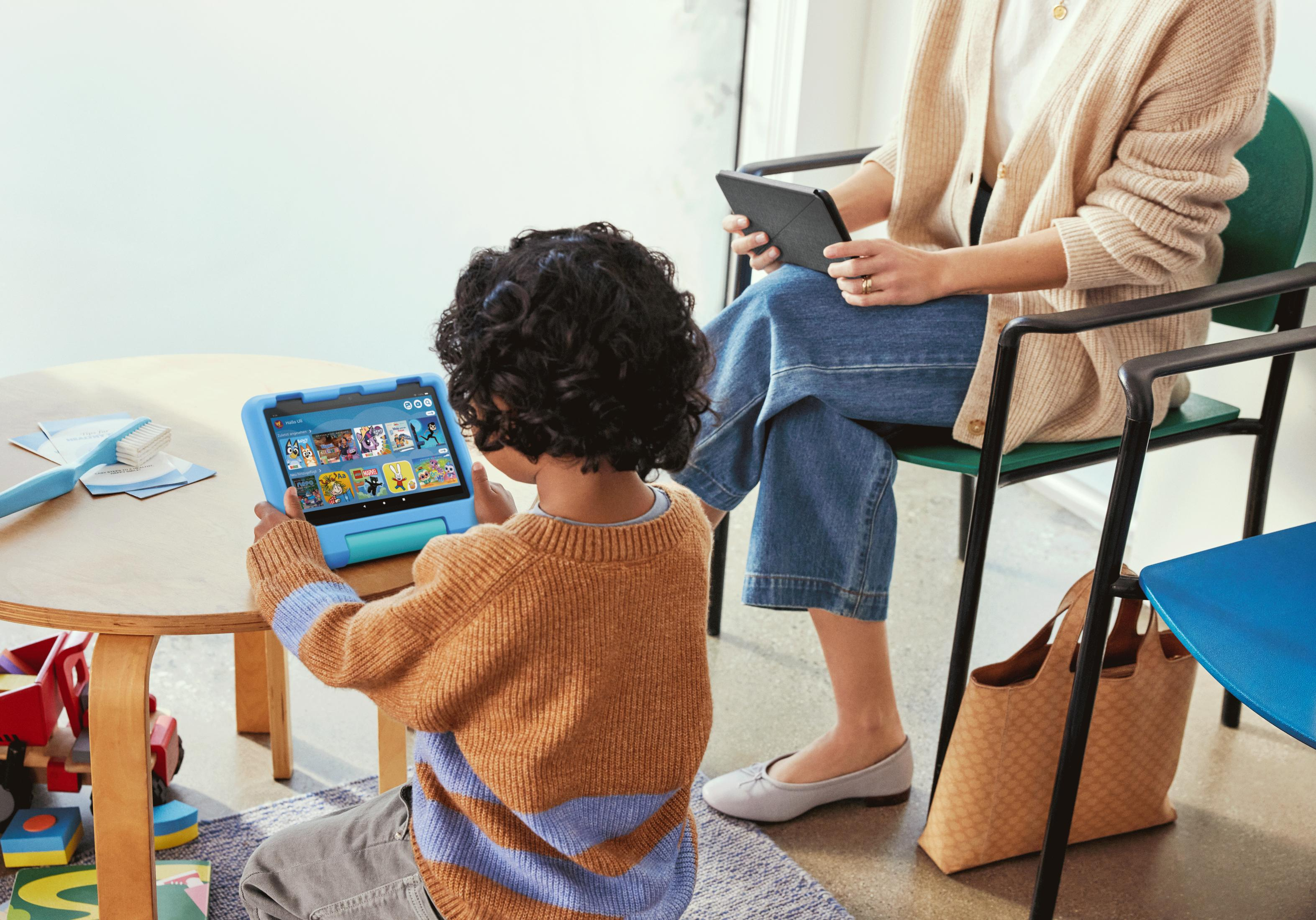 Ein Kind hält ein blaues Tablet, während es in der Nähe eines Erwachsenen mit einem anderen Tablet sitzt.