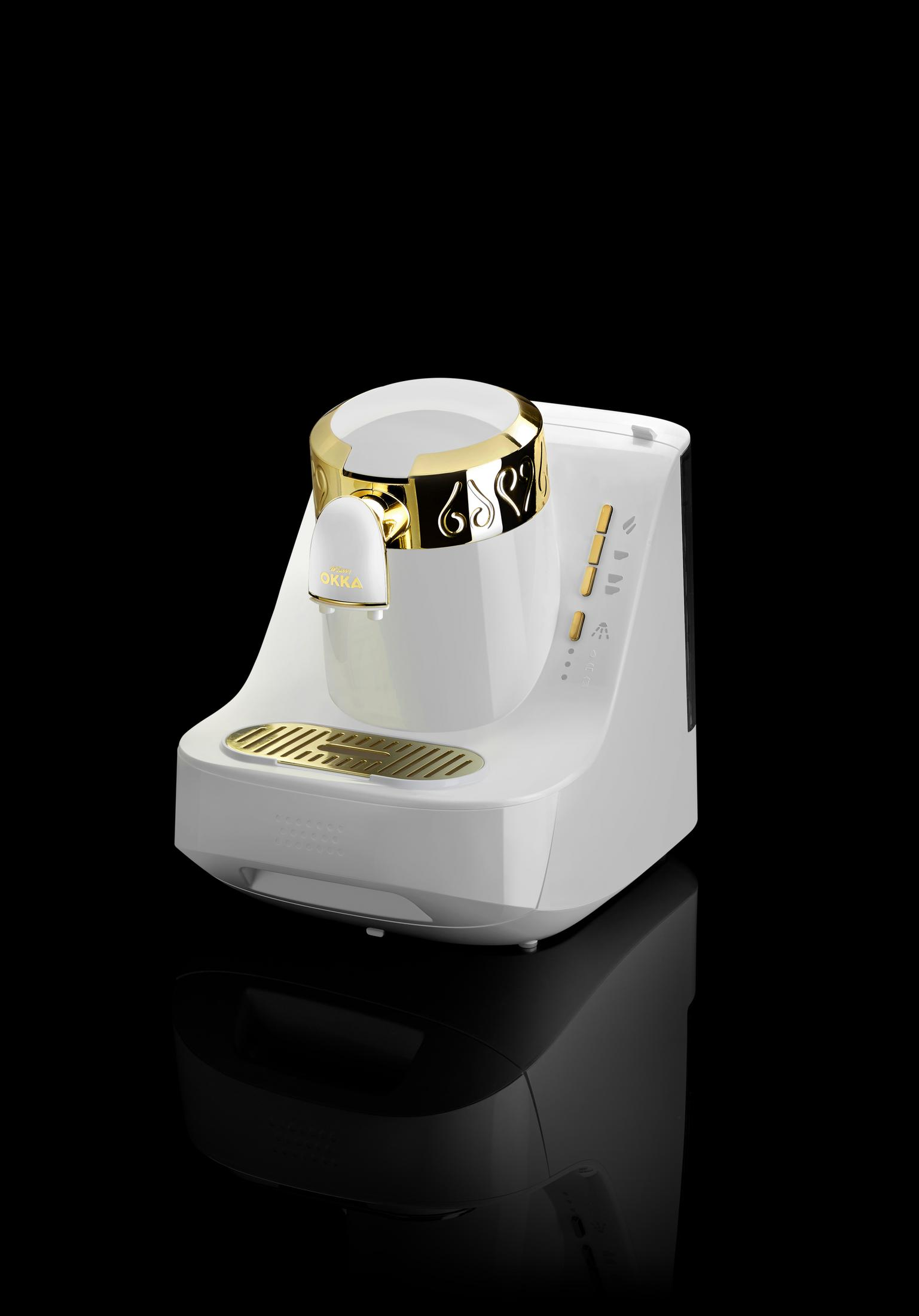 Ein weißer türkischer Kaffeeautomat mit goldenen Akzenten steht auf einer reflektierenden schwarzen Oberfläche.
