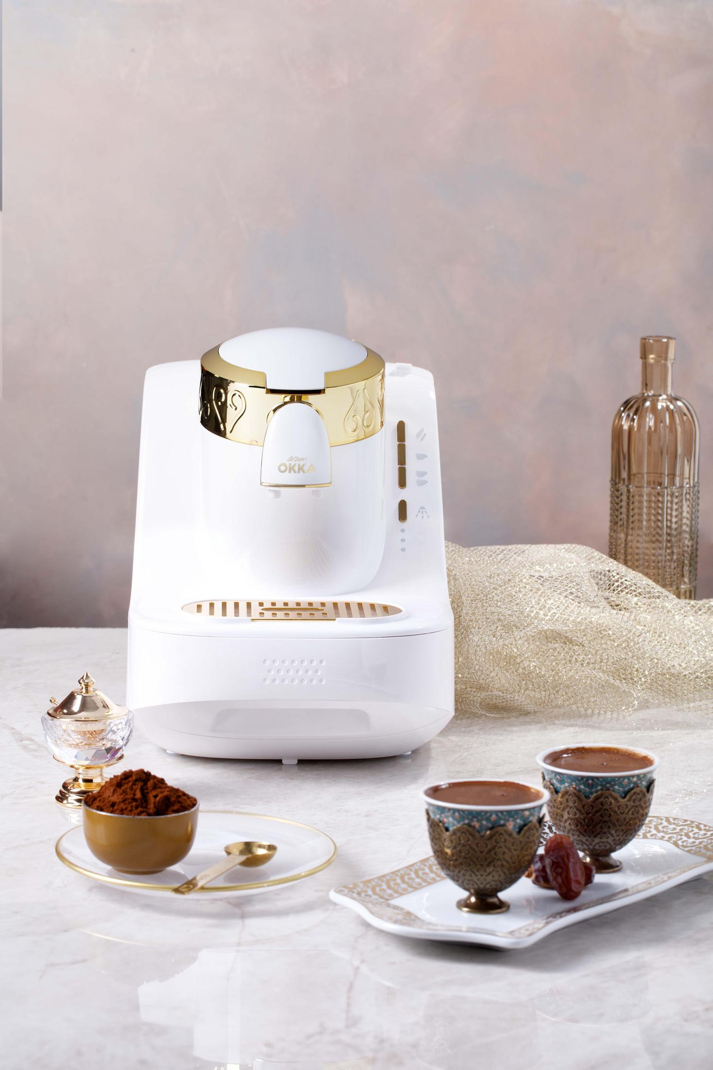 Weißer Kaffeebereiter mit goldenen Akzenten, Kaffeetassen und Kaffeepulver.