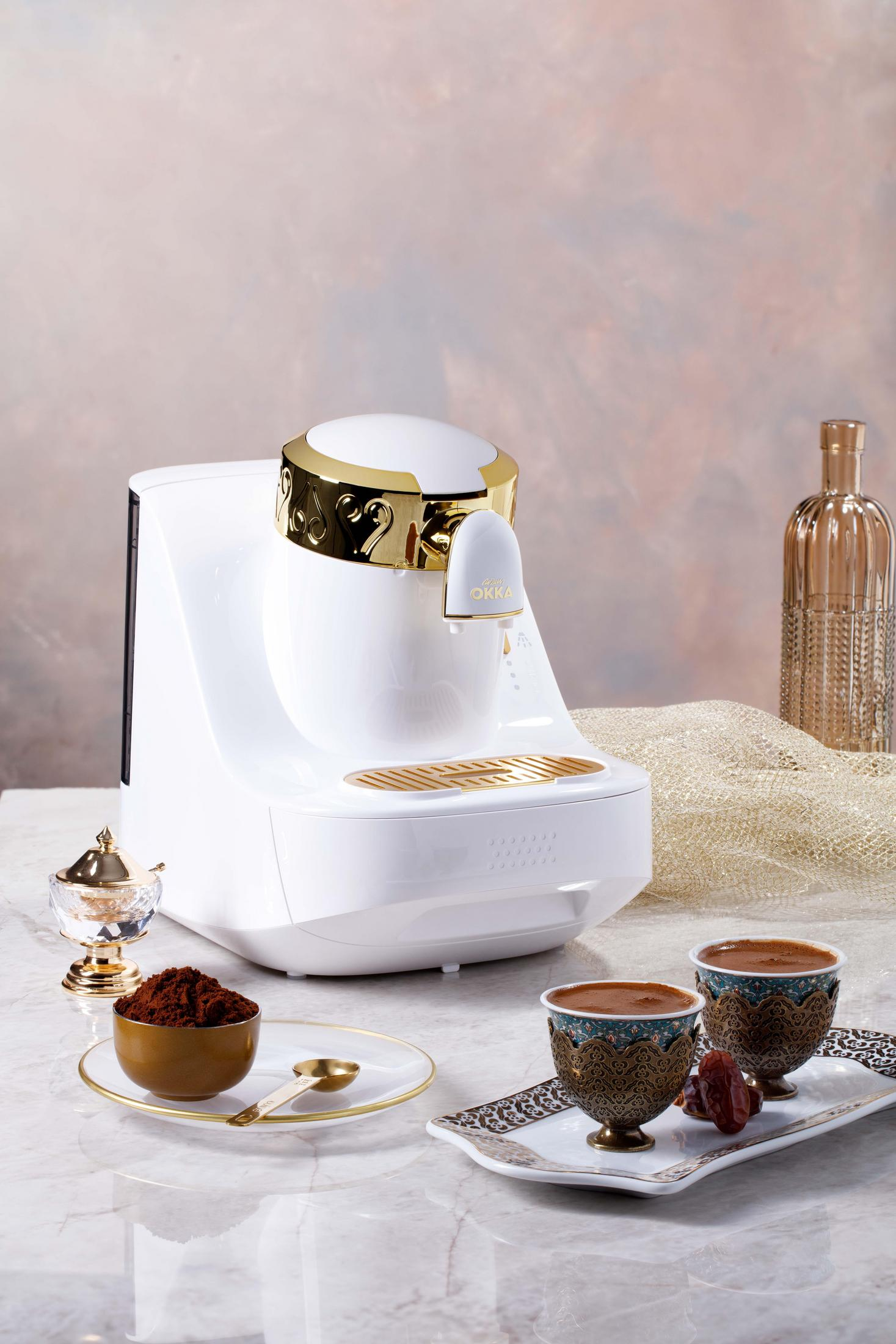 Weißer Kaffeebereiter mit goldenen Akzenten. Zwei Tassen Kaffee und Kaffeepulver.