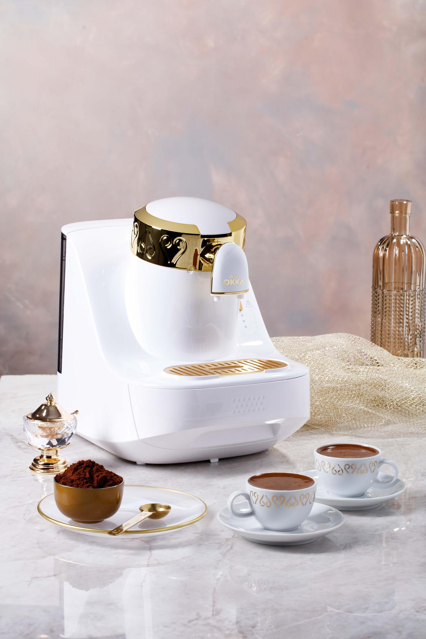 Weiße Kaffeemaschine mit Goldakzenten. Zwei Kaffeetassen auf einem Tablett.