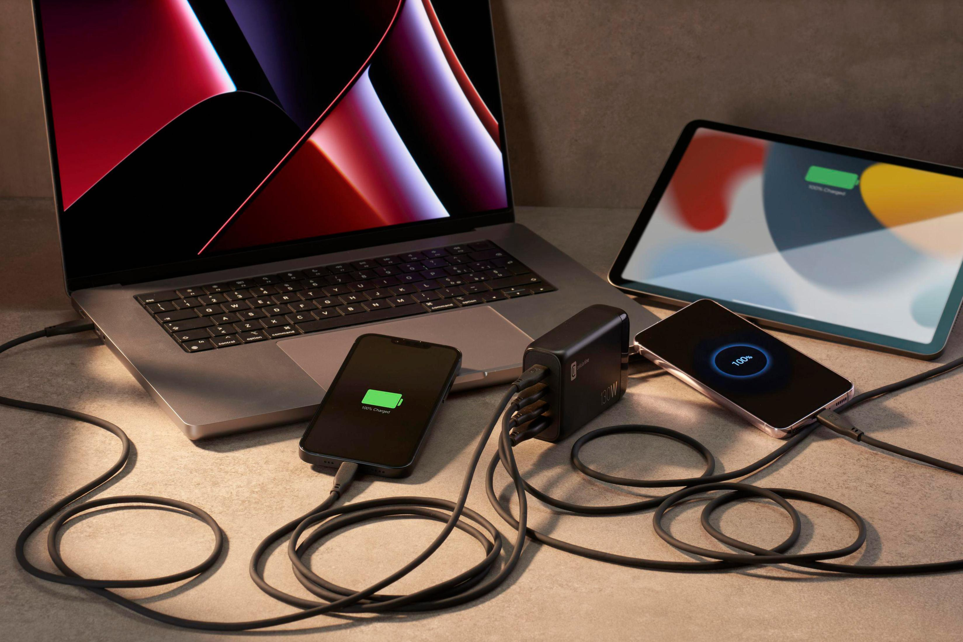 Ein Laptop, ein Tablet und zwei Telefone werden mit einem schwarzen Ladegerät und Kabeln auf einer Oberfläche aufgeladen.
