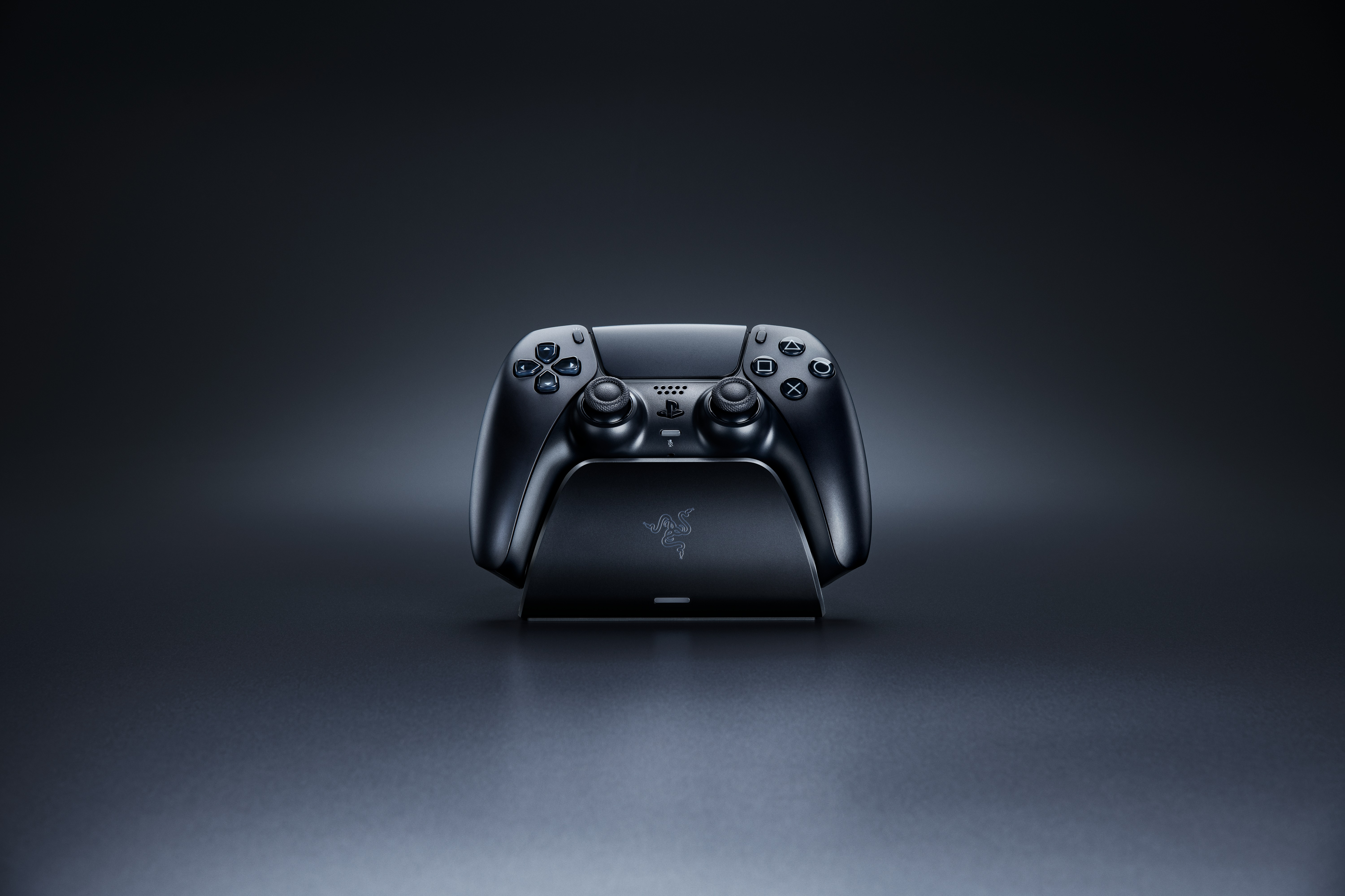 Karanlık bir arka plan önünde Razer şarj ünitesinde siyah bir PlayStation 5 oyun kolu, şık tasarımı sergileniyor.