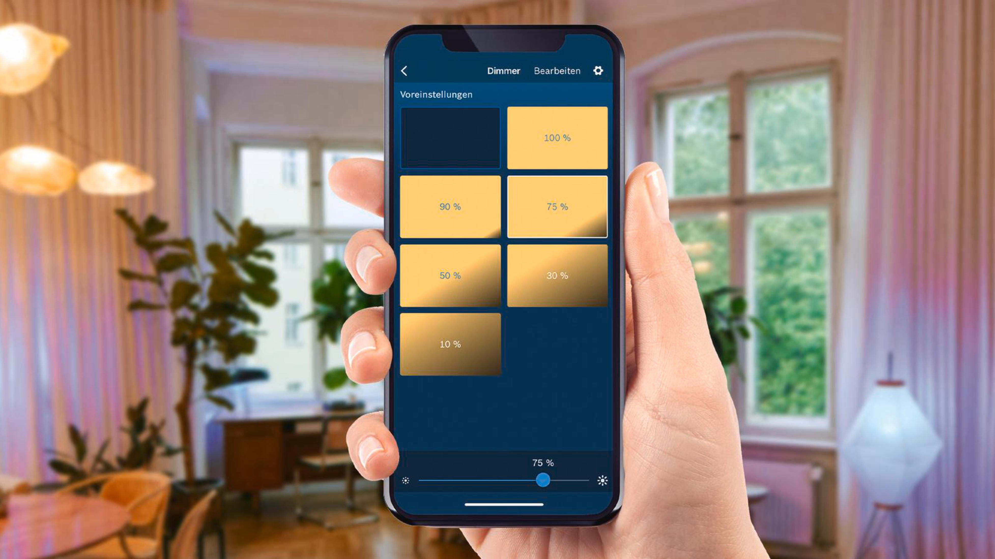 Eine Hand hält ein Telefon, das Dimmer-Einstellungen in einem Raum mit Lichtern anzeigt.
