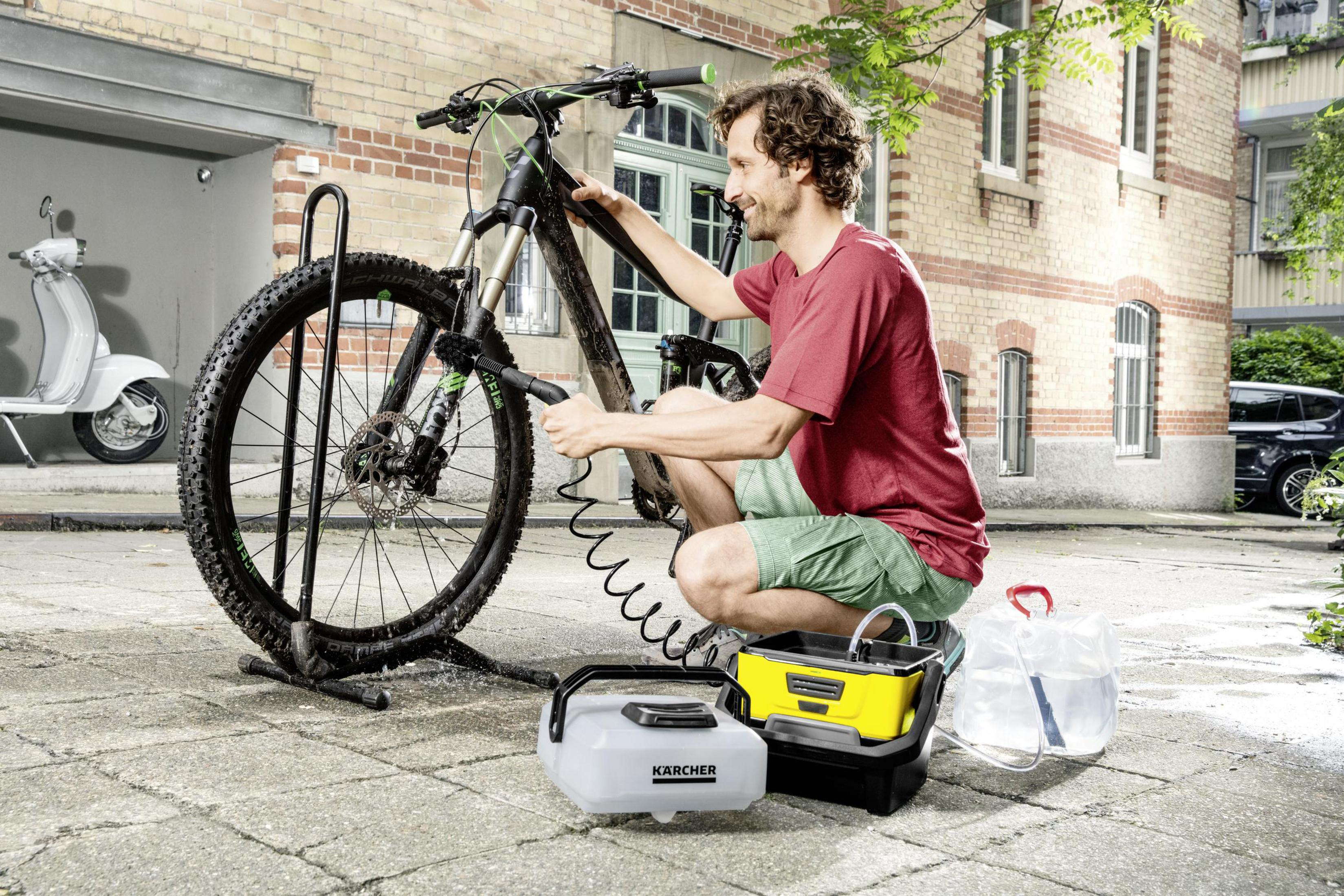 Uomo che pulisce una mountain bike con una spazzola e un sistema di pulizia in un ambiente urbano.