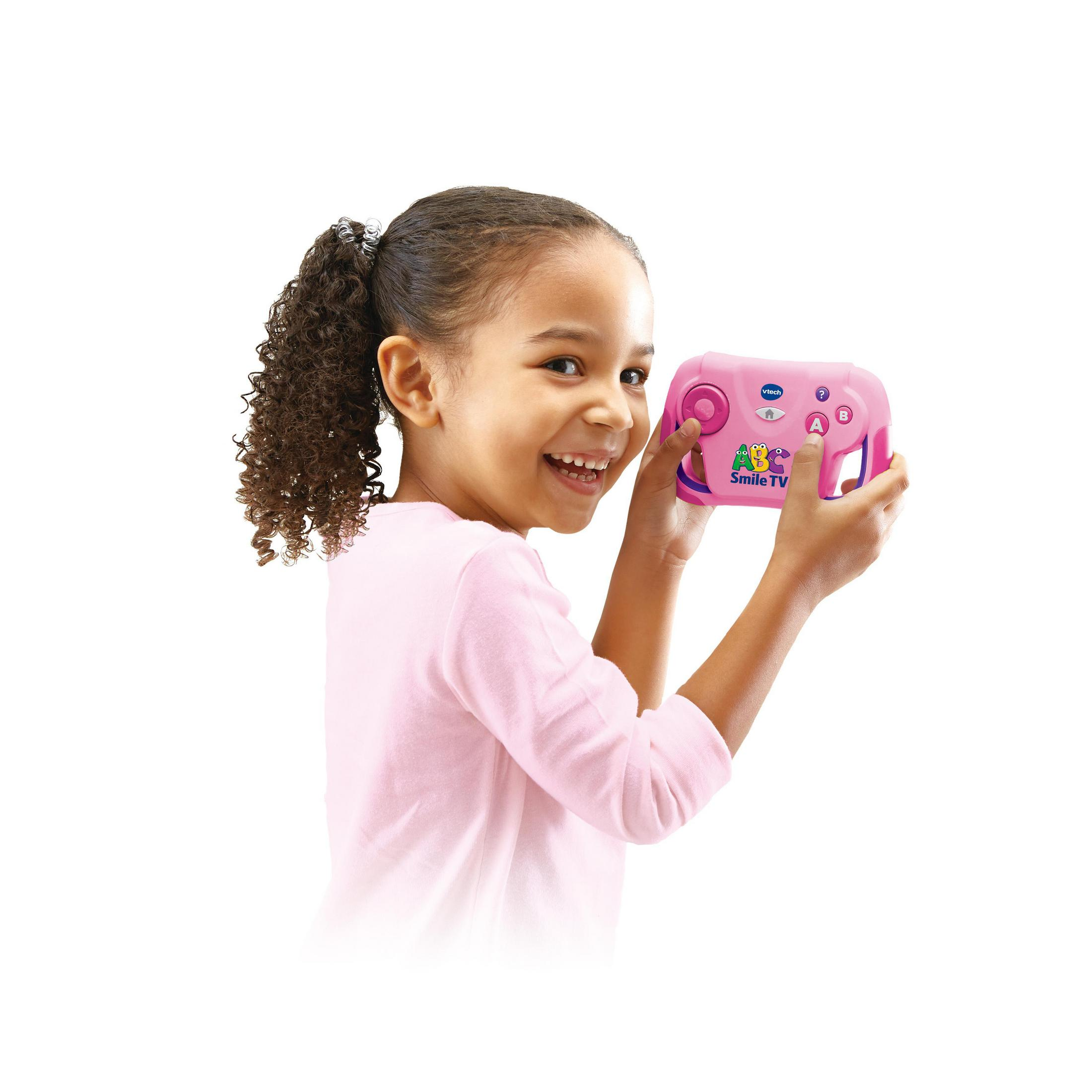 Ein lächelndes Mädchen hält einen rosa VTech ABC Smile TV-Controller vor einem weißen Hintergrund.