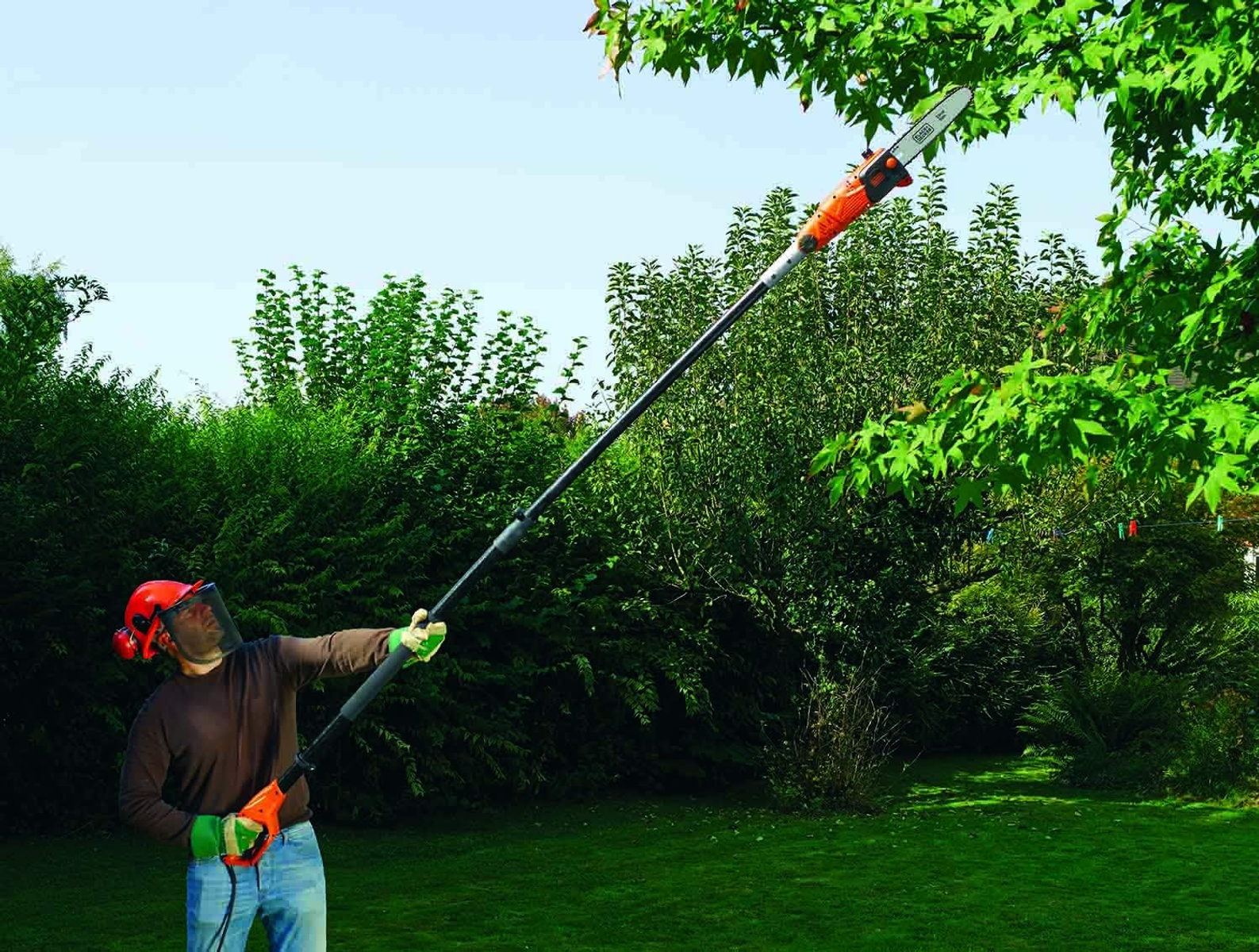 Osoba używa piły na wysięgniku do cięcia gałęzi drzewa w słoneczny dzień w ogrodzie.